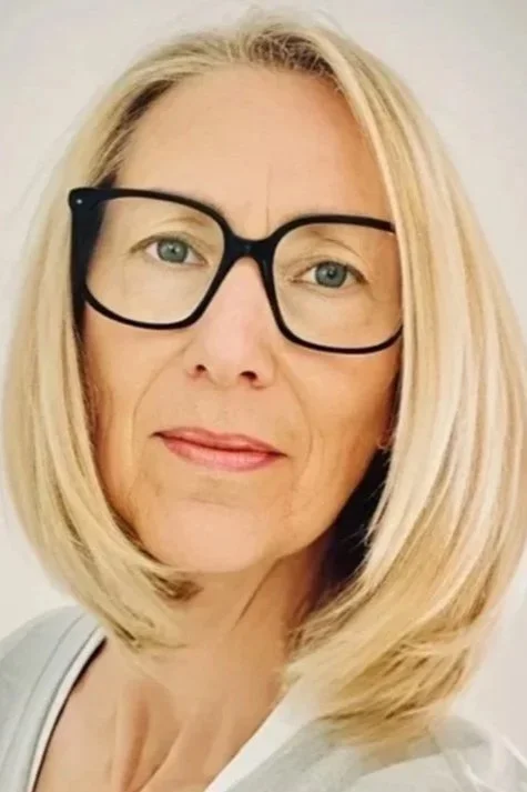 Nahaufnahme einer Frau mit blondem Haar, schwarzer Brille und einem weißen Oberteil