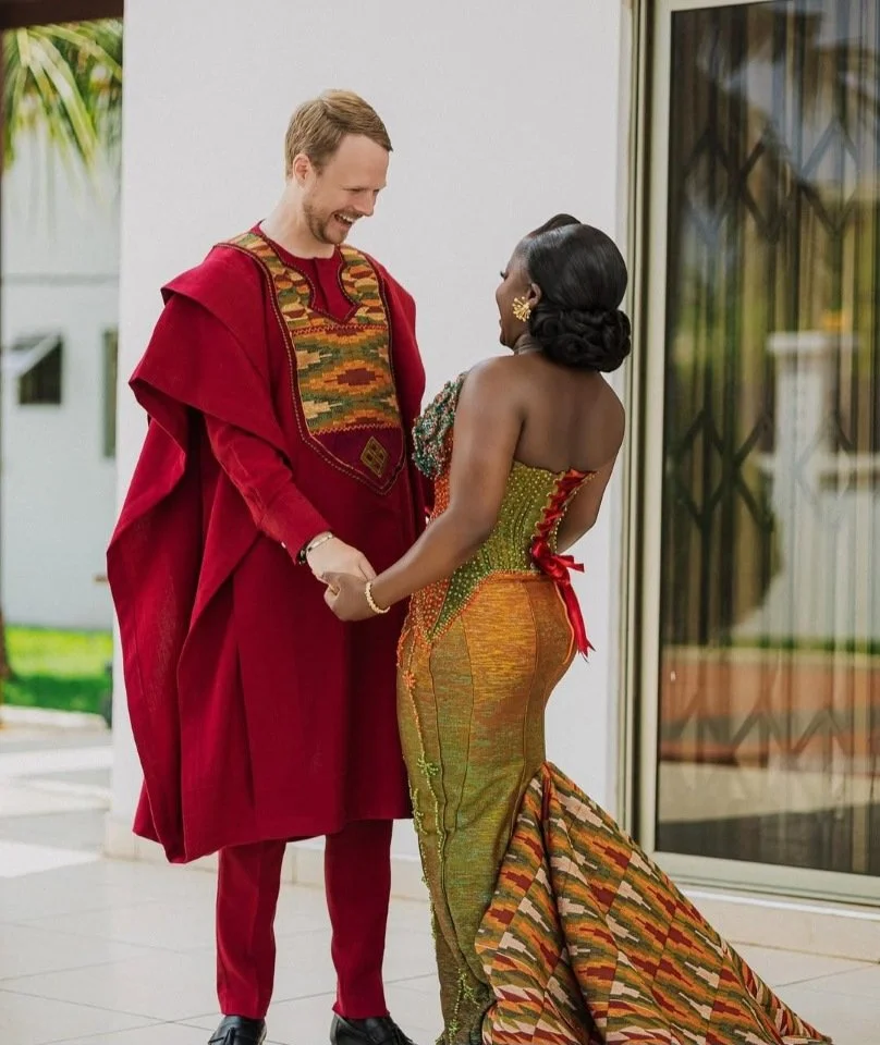 Een man en een vrouw die hand in hand staan, lachend naar elkaar onder een overhangende boog in een lichte ruimte met een glazen deur en groene planten buiten.