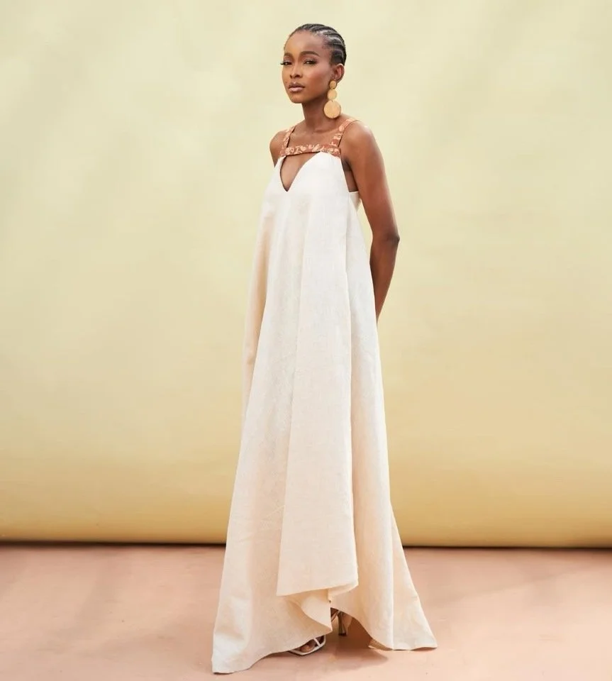 Vrouw in witte avondjurk met gouden oorbellen op een beige achtergrond.