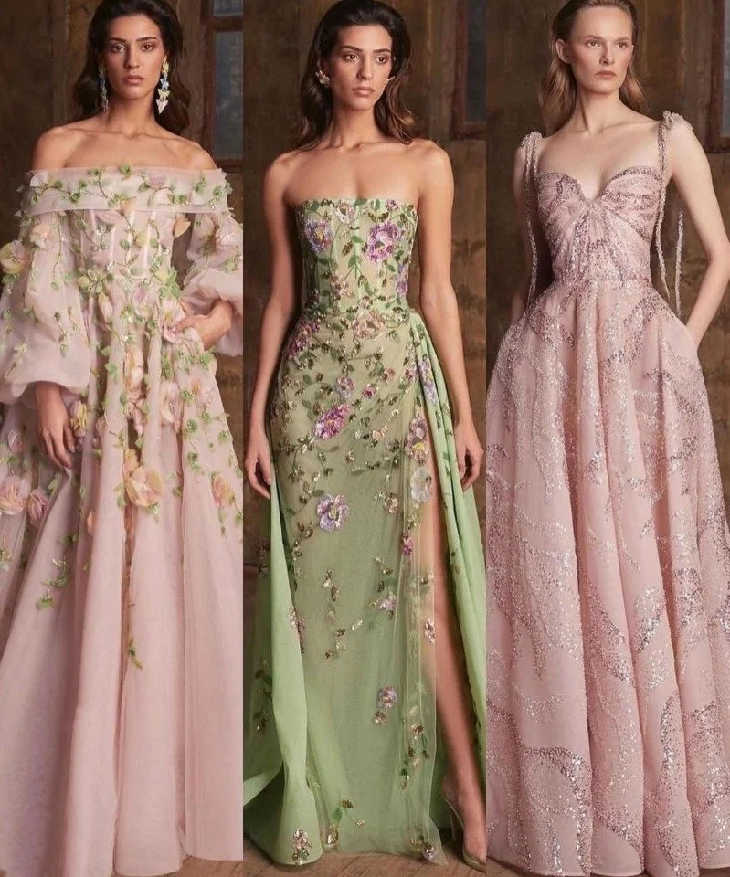 Drie vrouwen dragen elegante, bloemrijke avondjurken in pasteltinten.