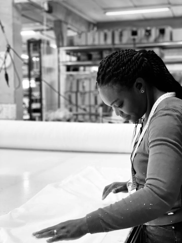 Vrouw die in een werkplaats of atelier bezig is met naaien of stoffen snijden.