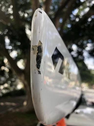 Close-up of a damaged white car side mirror with scratches and missing paint