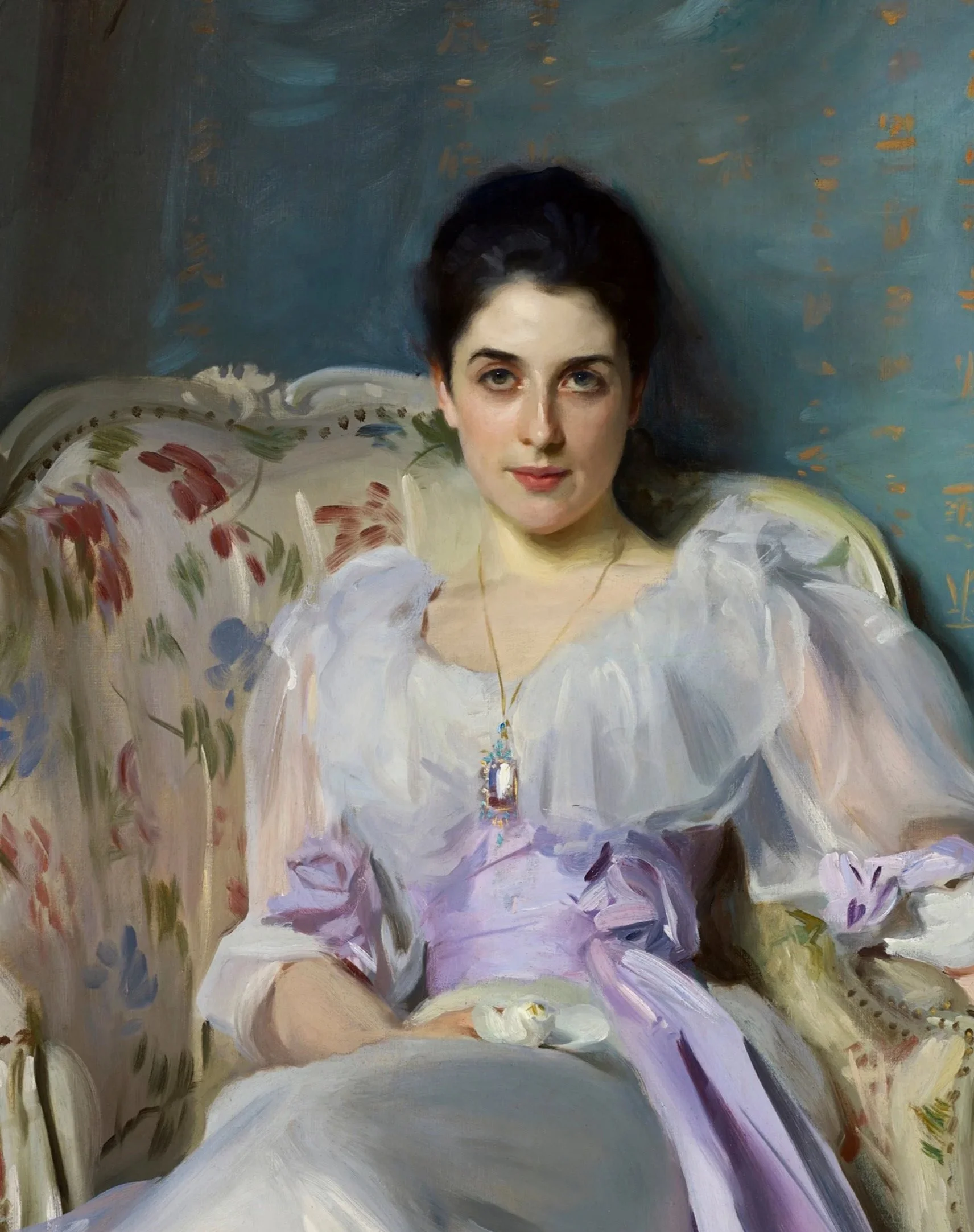 Retrato de una mujer con cabello oscuro y vestimenta elegante, sentada en un sillón adornado con cojines de flores, en un fondo colorido y artístico.