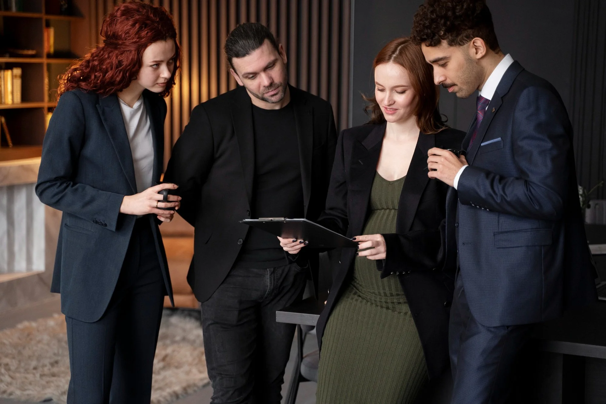 Cinco pessoas de traje empresarial analisando documentos em um ambiente de escritório moderno.