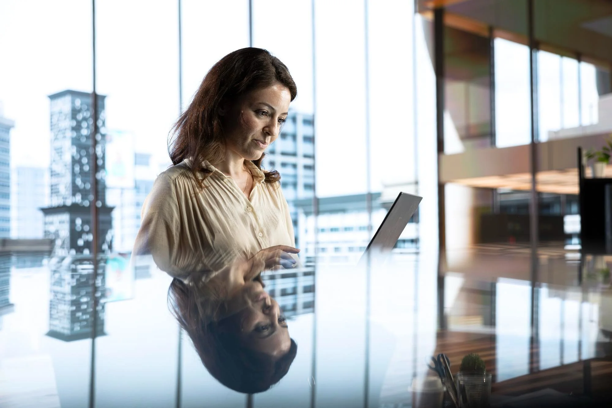 Mulher usando um tablet em um escritório com janelas grandes e vista para prédios.