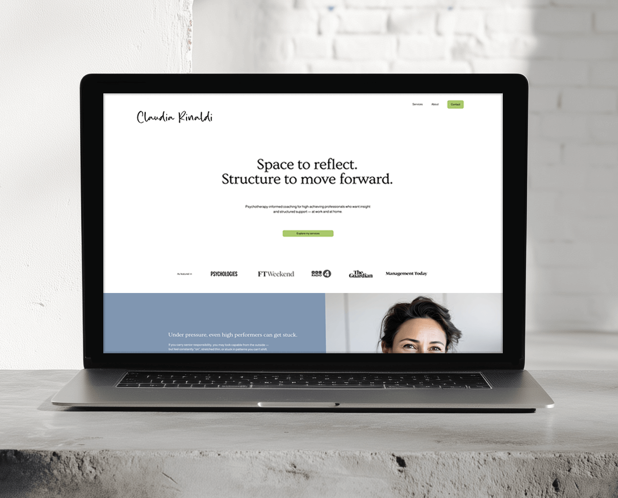 Laptop on concrete surface displaying a website with text about therapy and coaching, a profile picture of a woman, and several media logos at the bottom.