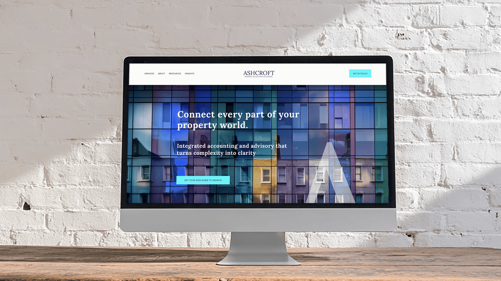 An iMac computer displays a website for Ashcroft Property Accounting & Advisory with a background of colorful apartment buildings and the text 'Connect every part of your property world' on a white brick wall background.