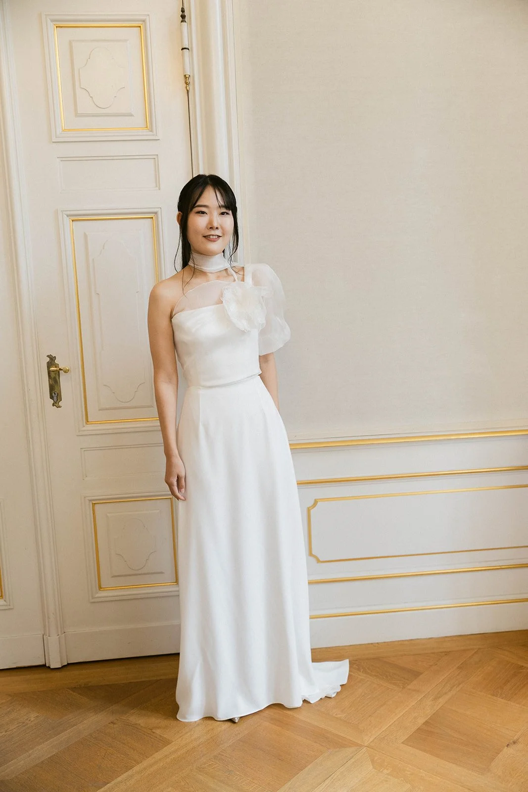 A woman in a white dress standing in a room with elegant decor and wood flooring. Documentary and loose editorial style wedding photography.