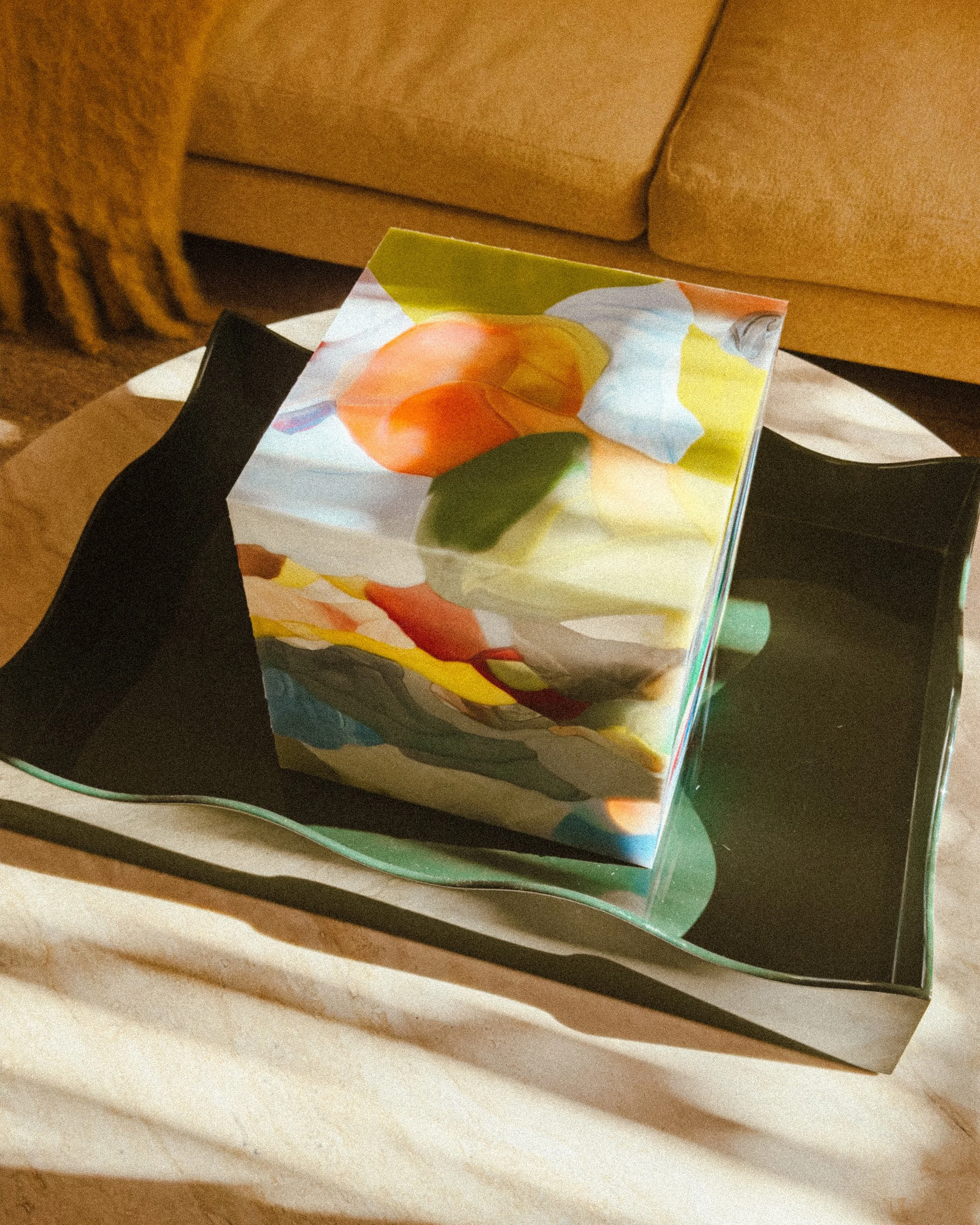 A glass cube with colorful abstract patterns inside, placed on a decorative tray.