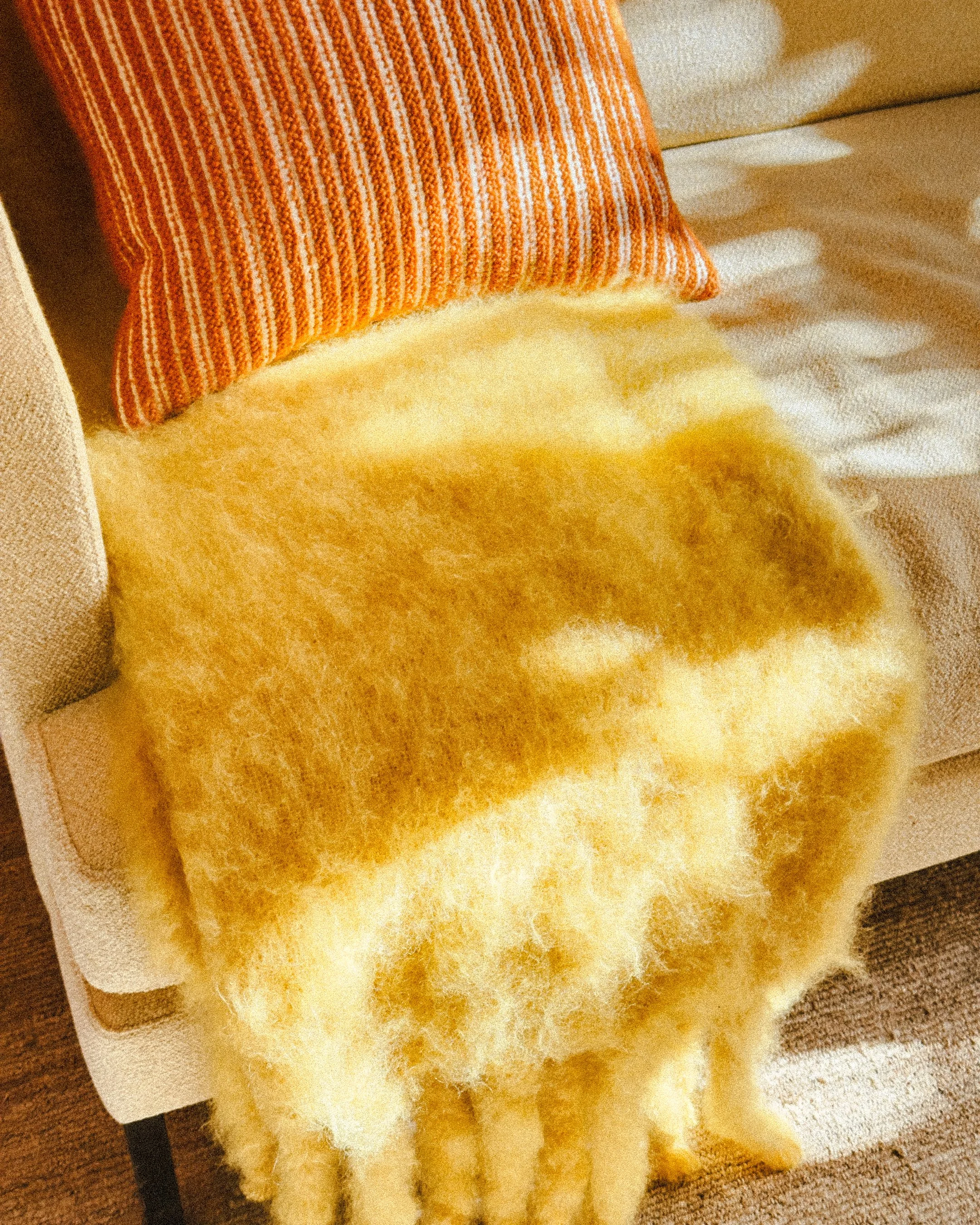 Close-up of a cozy beige upholstered armchair with an orange striped pillow and a soft yellow throw blanket.