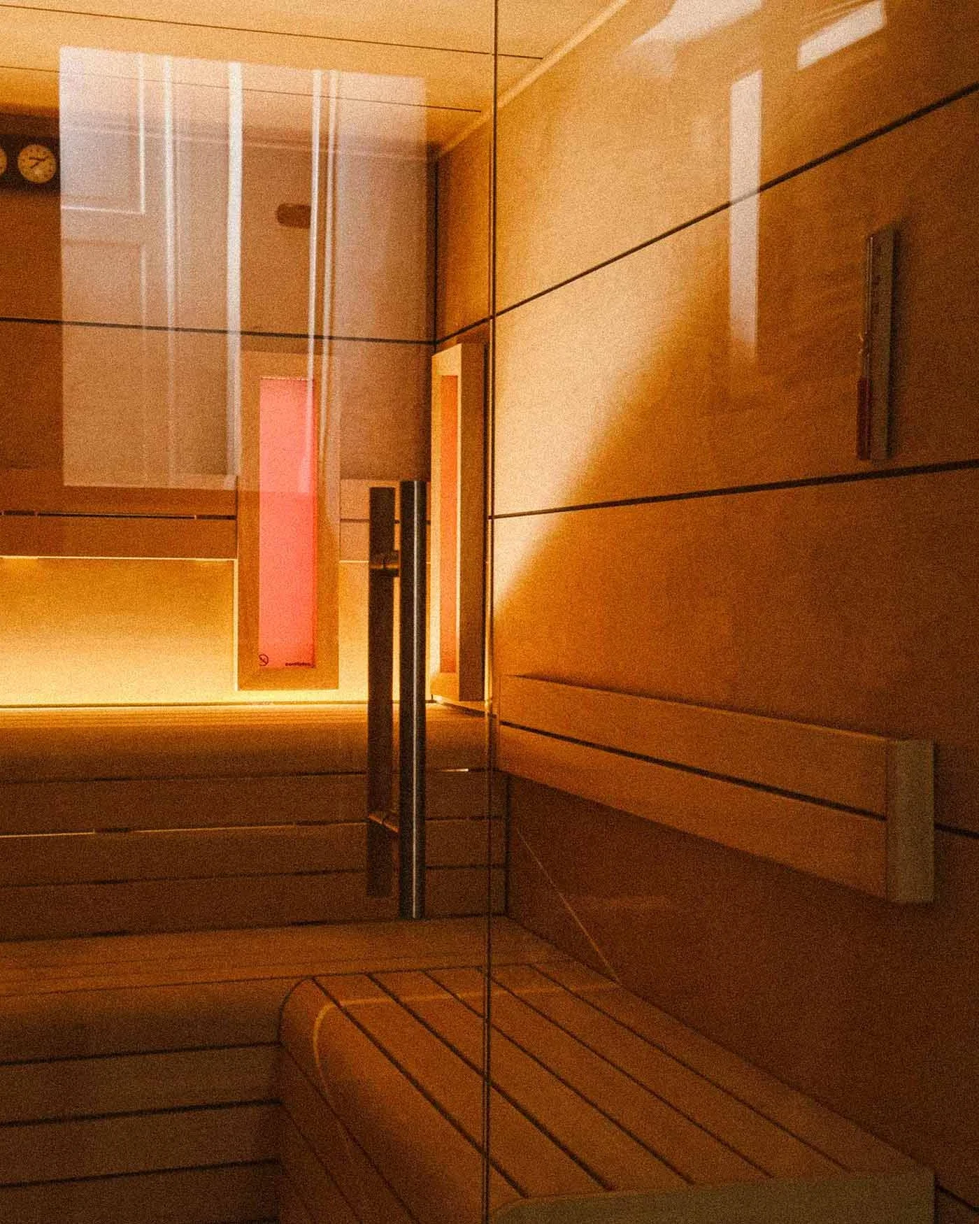 Interior of a modern sauna with wooden walls, benches, and a glass door, illuminated softly.