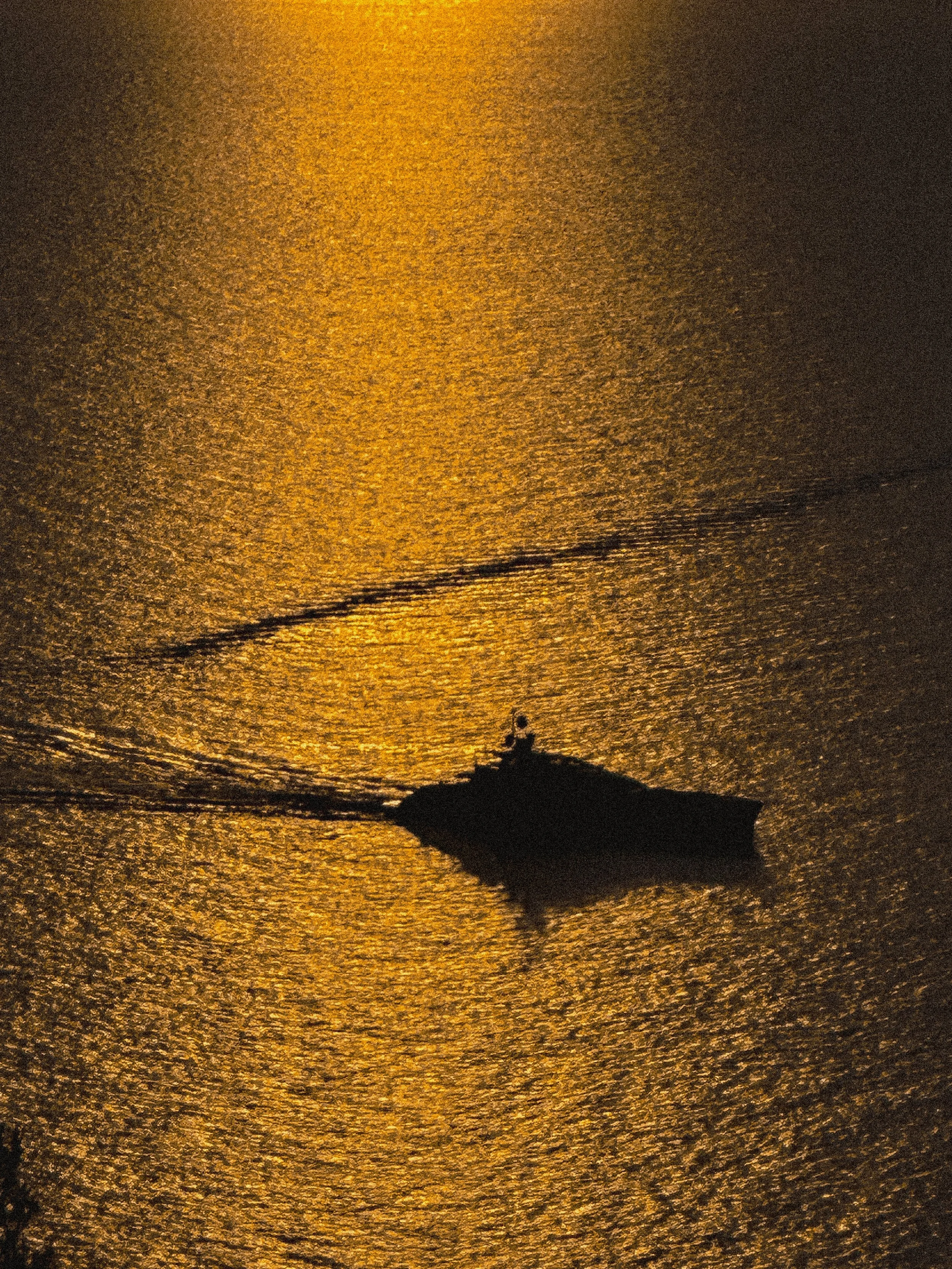 Silhouette of a boat on the water during sunset, with the sunlight reflecting on the surface.
