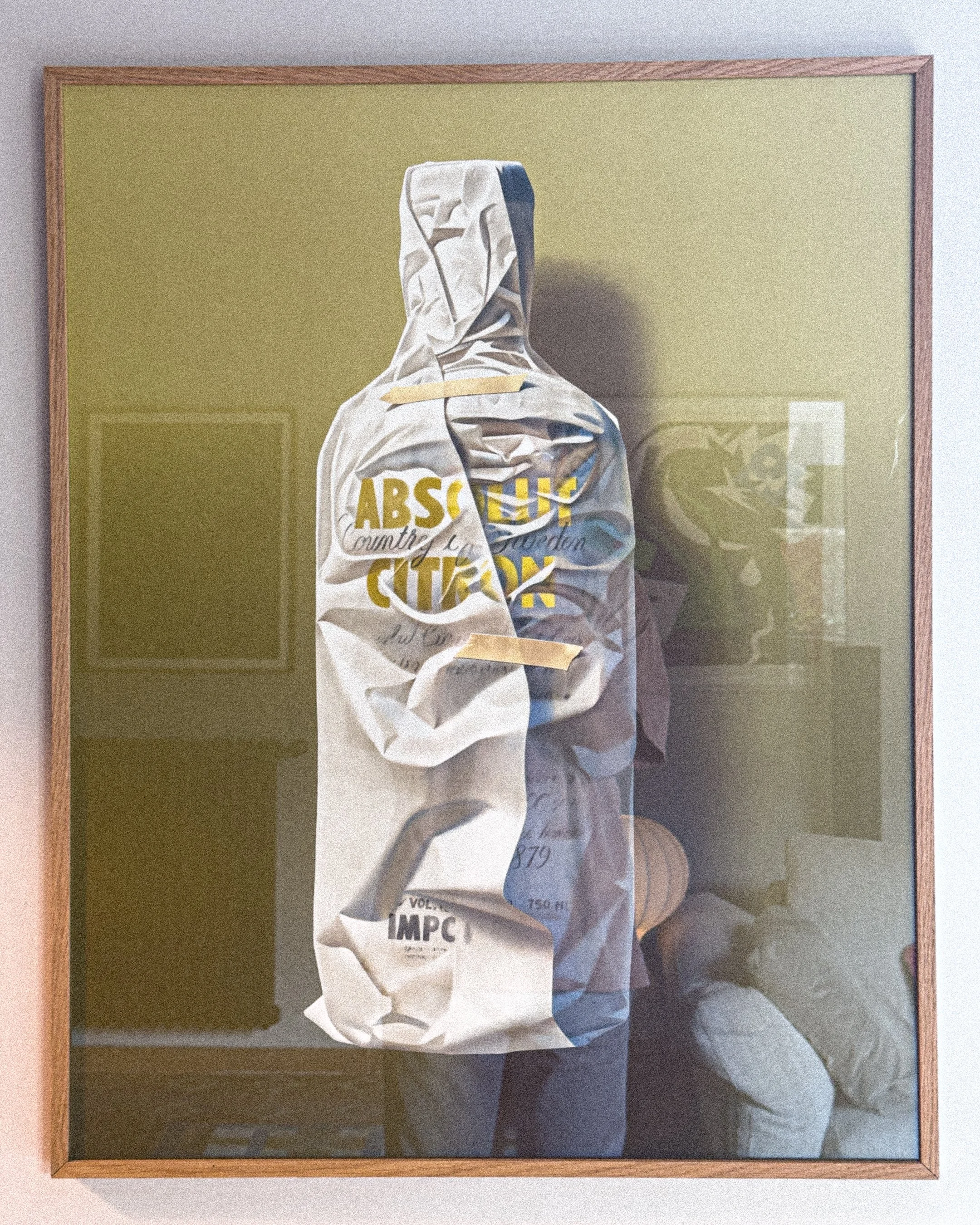 Framed art piece displaying a crumpled plastic bag with yellow and black text, with a reflection of a room in the glass.