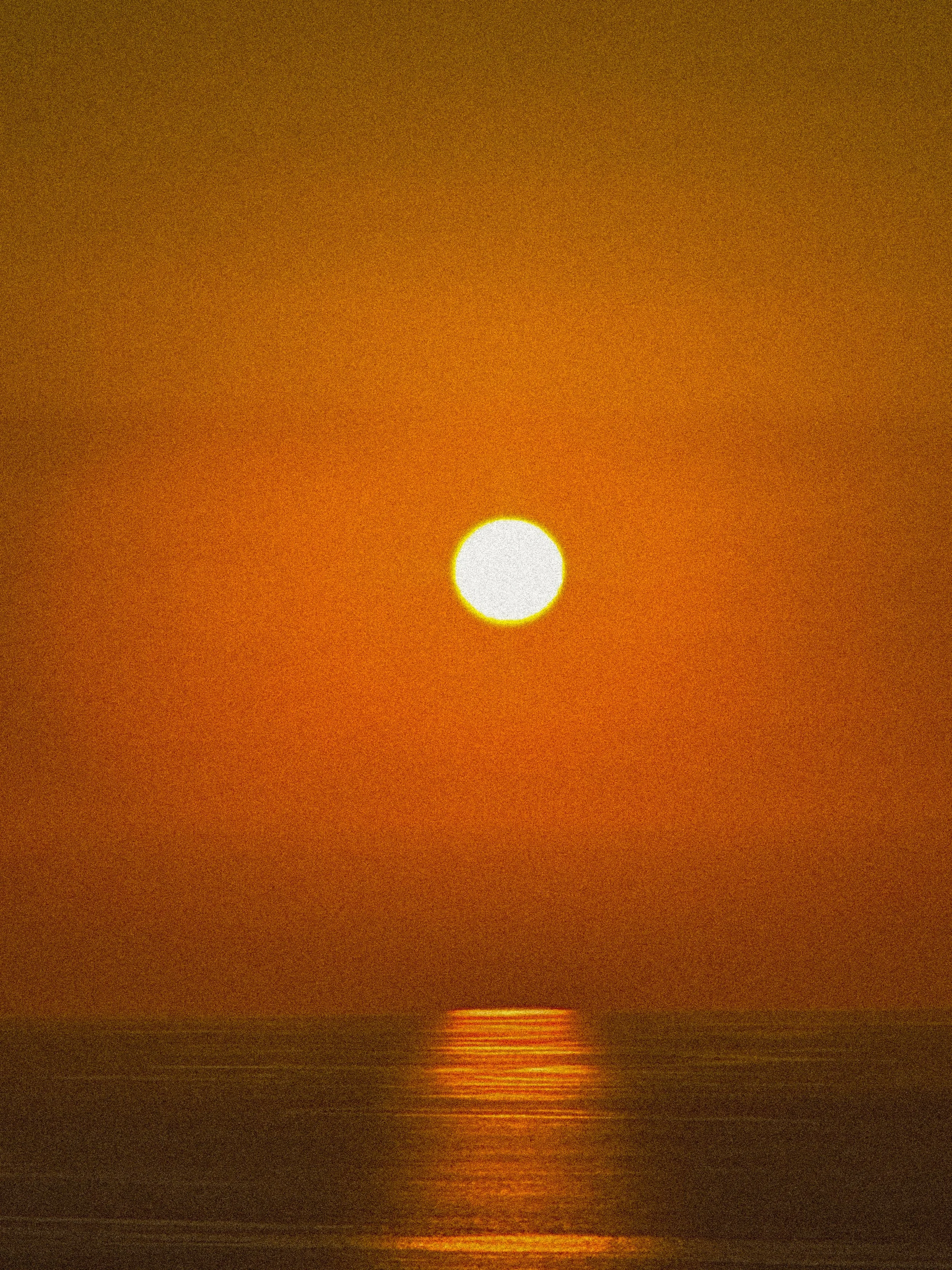 A large, bright sun setting over the ocean with a reflection on the water, during sunset or sunrise