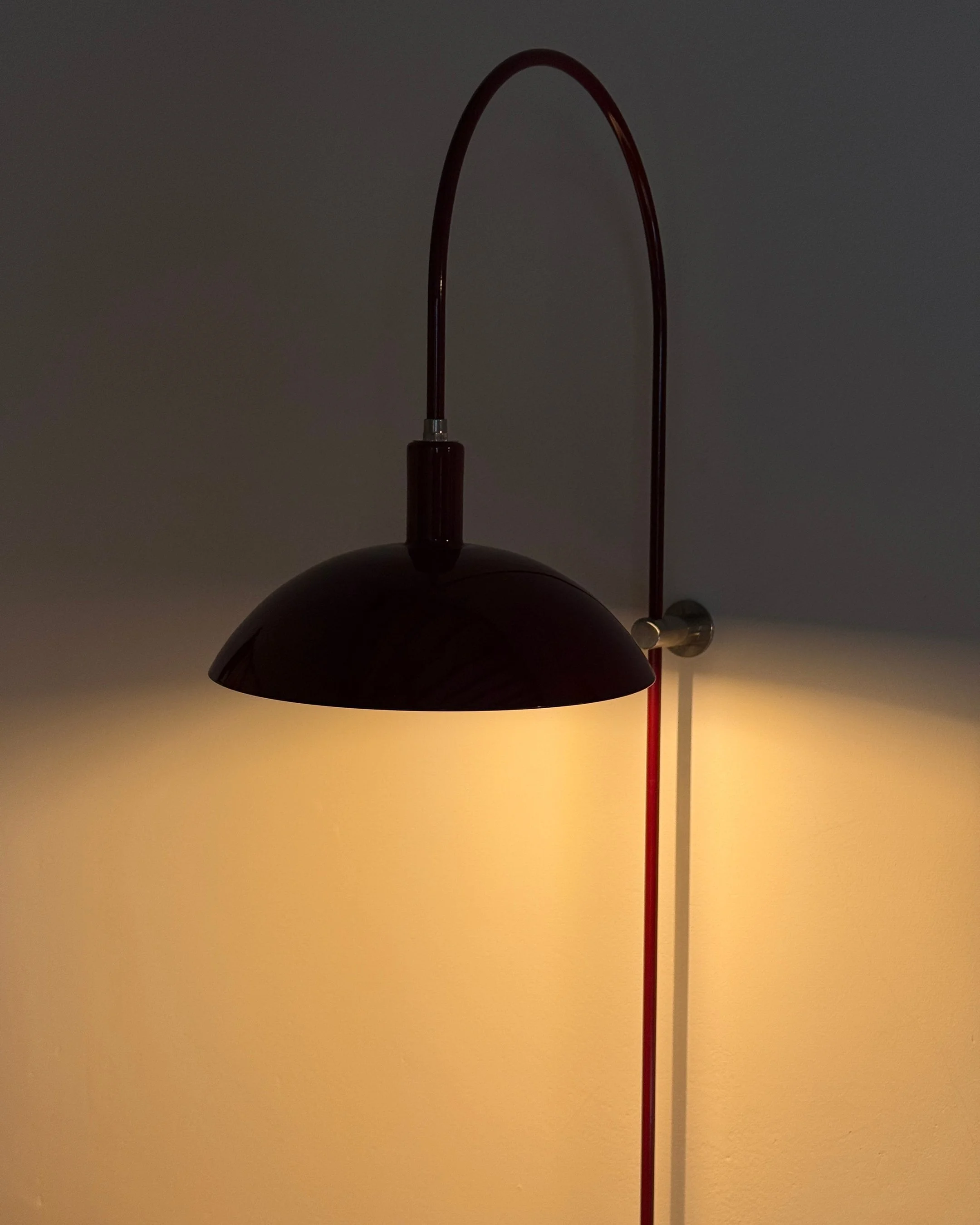 A modern wall-mounted lamp with a curved arm and a dark shade, casting warm light on a beige wall.