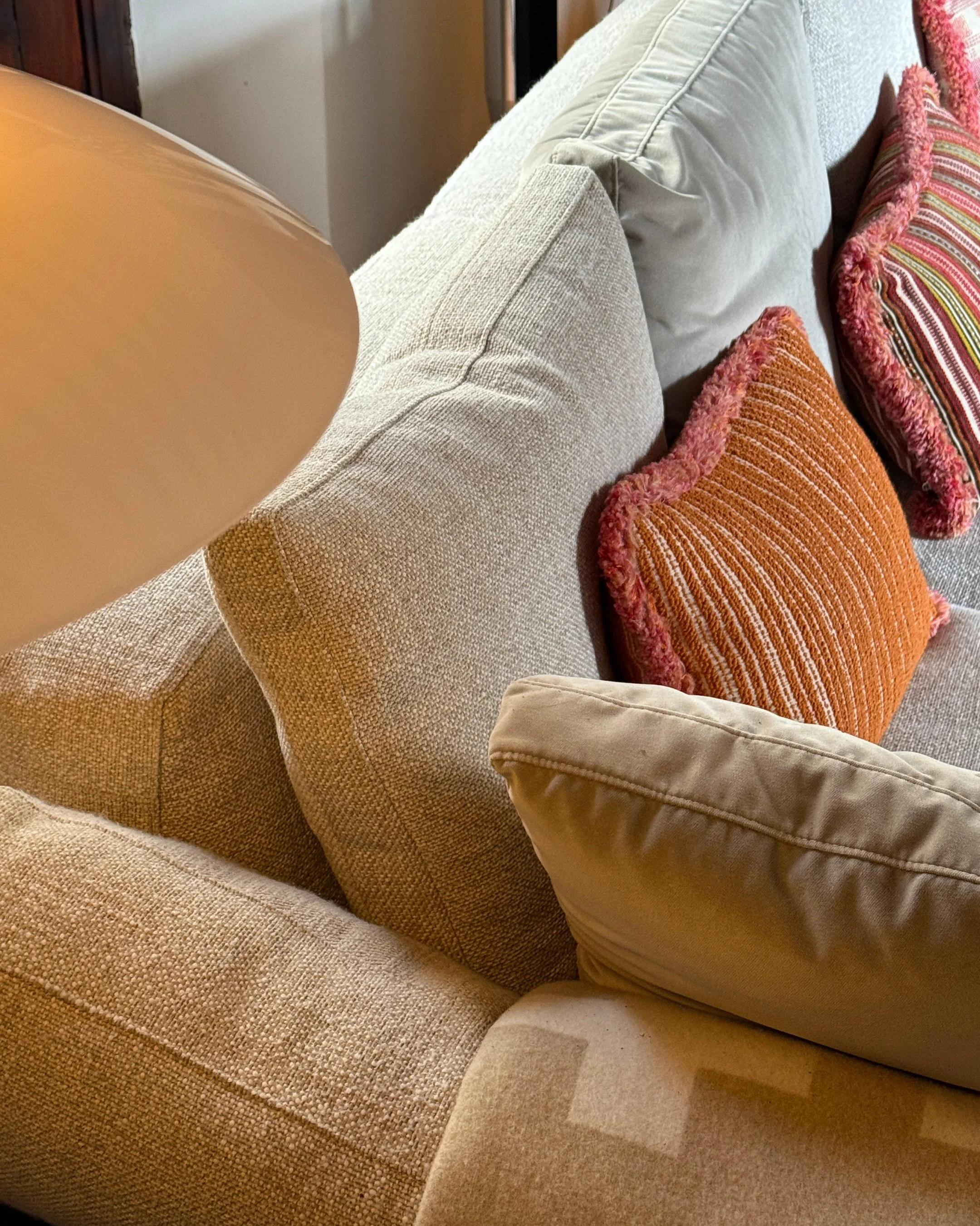 A beige sofa with various pillows, including an orange, pink, and striped pillow.