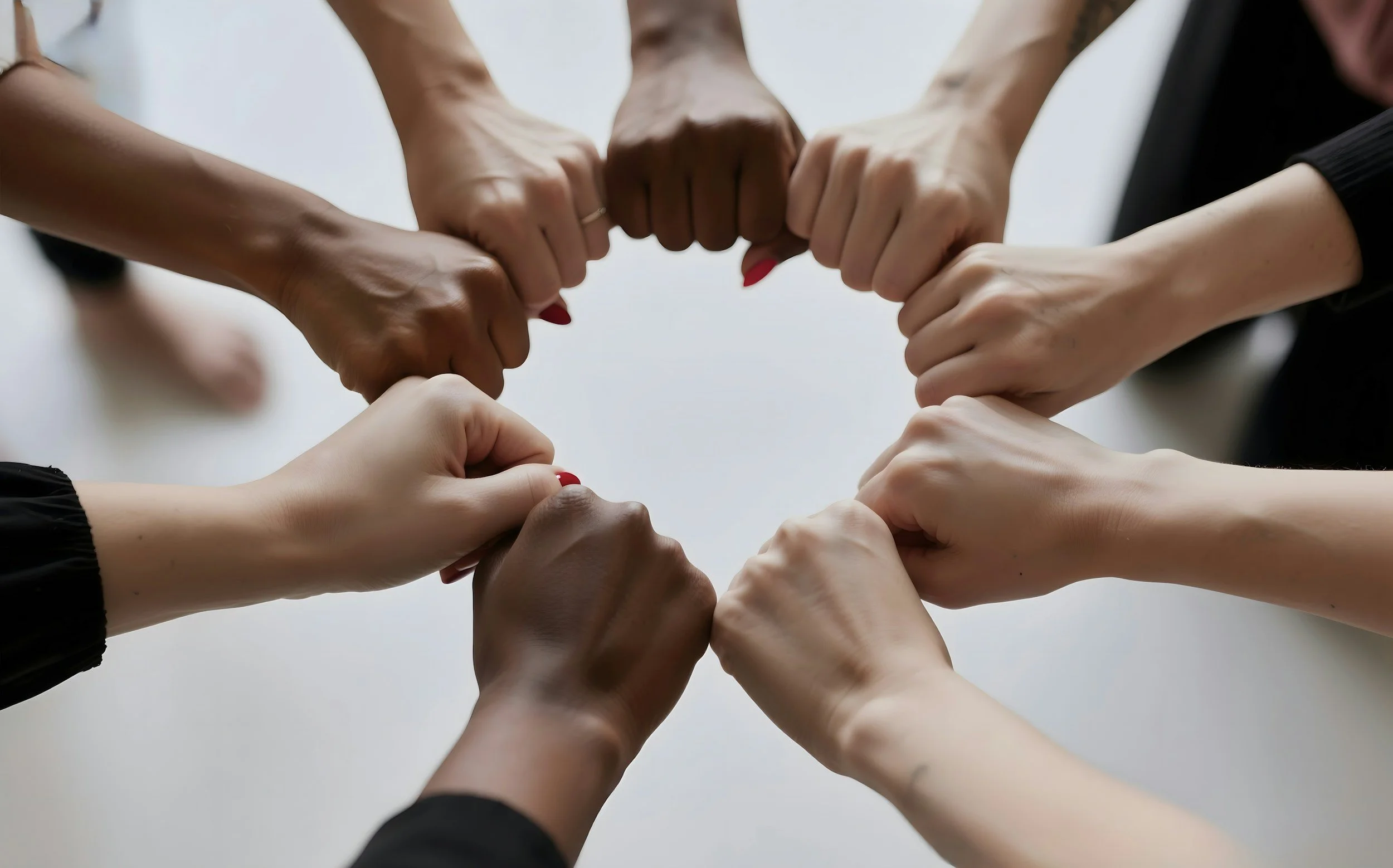 Multiple hands from diverse individuals forming a circle with fists touching in the center.