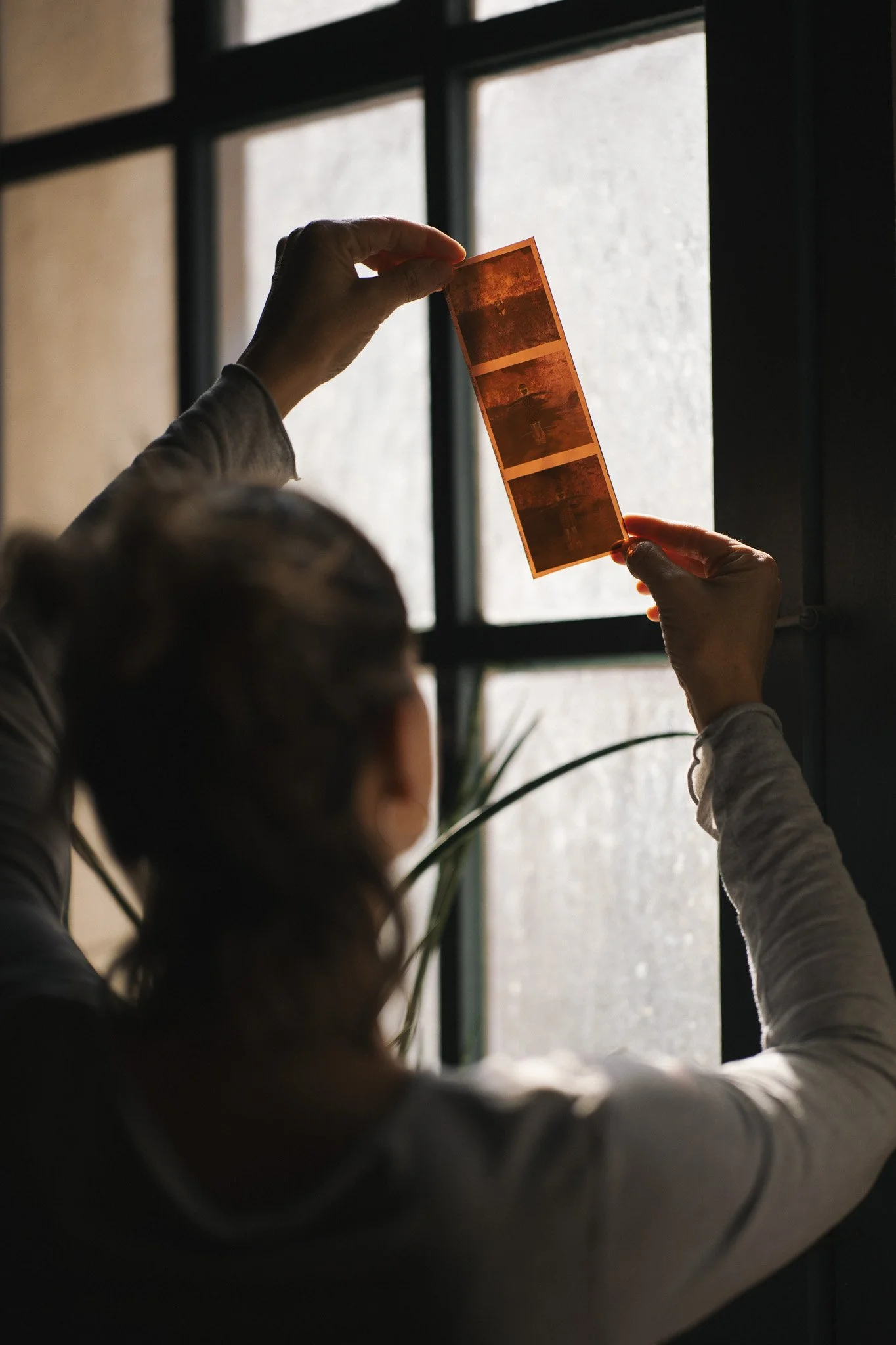 Person holding a strip of photo booth pictures near a window with frosted glass.