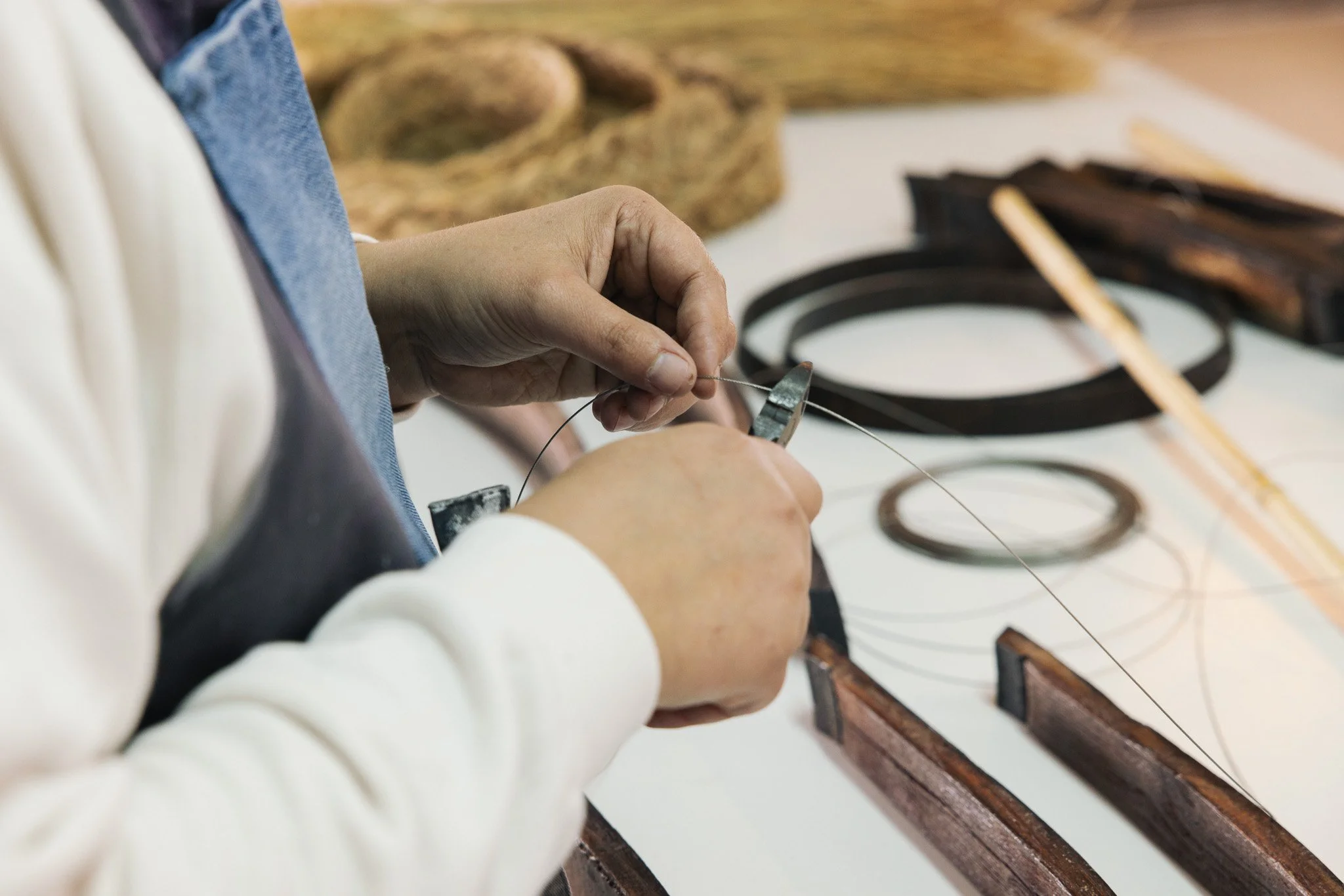 A person working with a thin wire, possibly for jewelry or watch repair, at a workspace with tools and wooden frames.