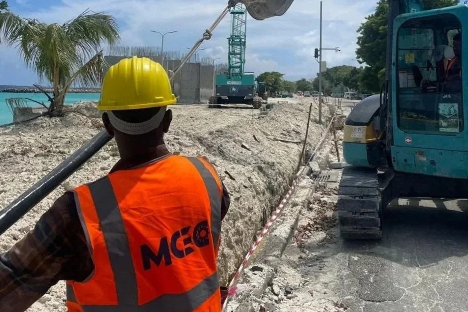Construction workers on a beach site with concrete blocks and equipment, ocean in the background.