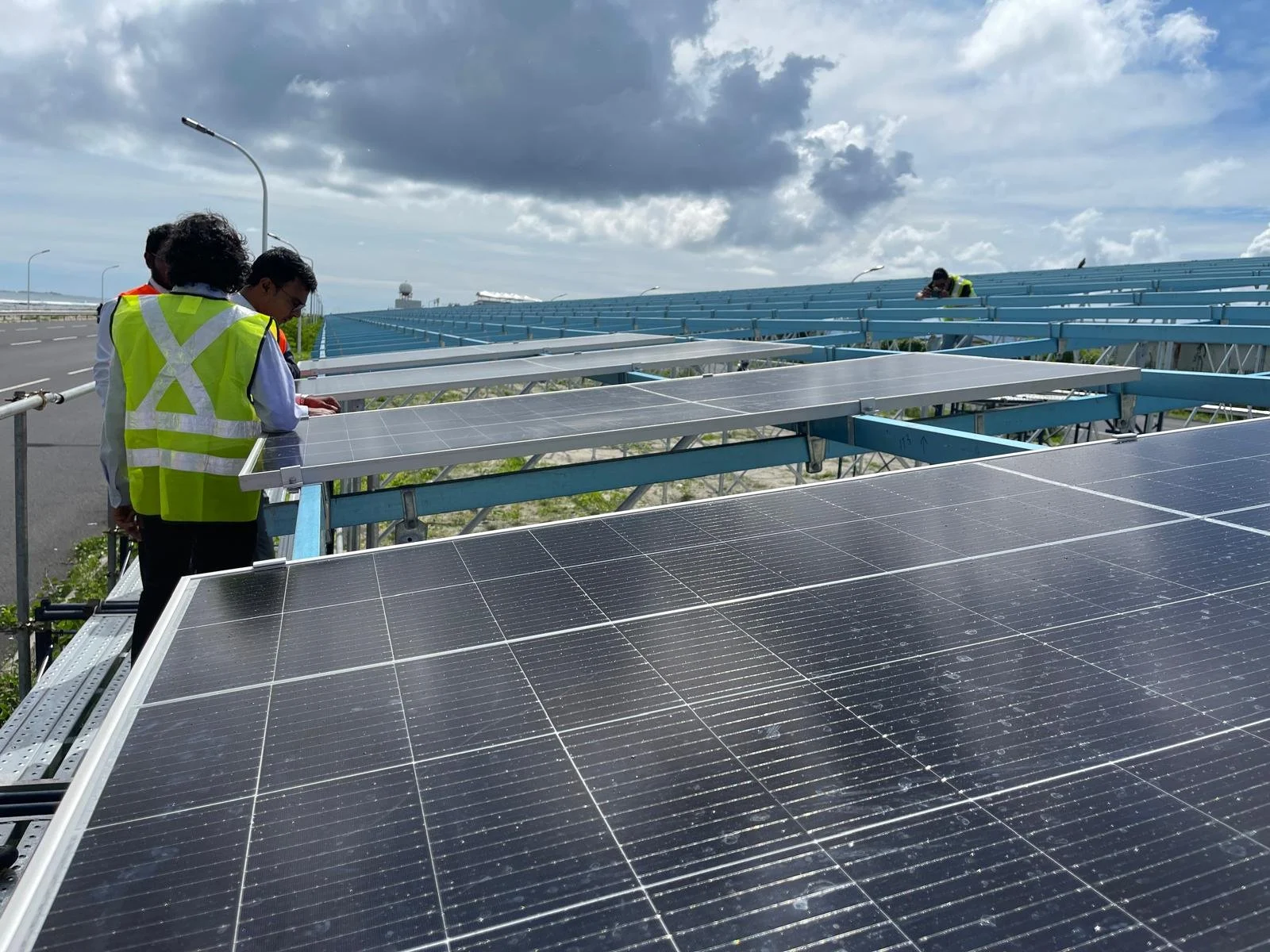 Group of workers inspecting solar panels on a large solar farm, with a cloudy sky in the background.