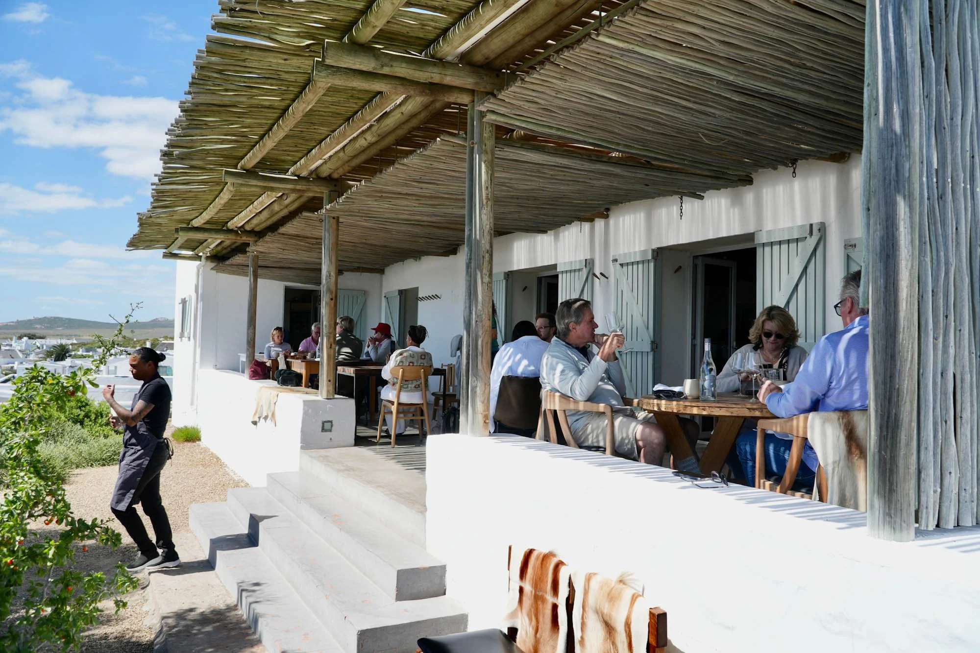 Gasten op een zonnig restaurantterras met rieten overkapping in Paternoster.