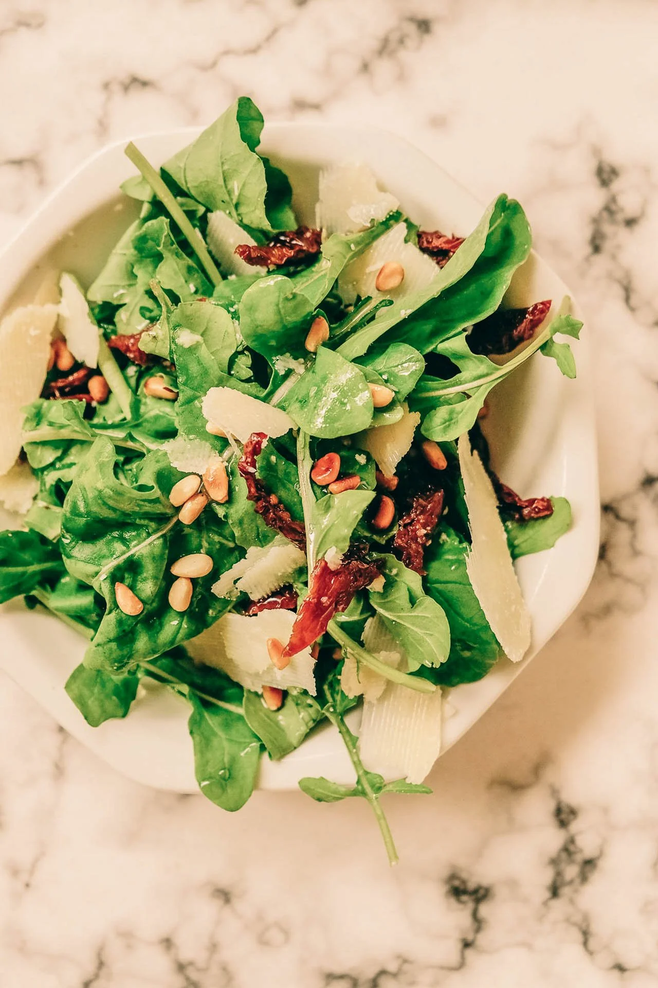 Bord met salade van rucola, zongedroogde tomaten, pijnboompitten en parmezaan.