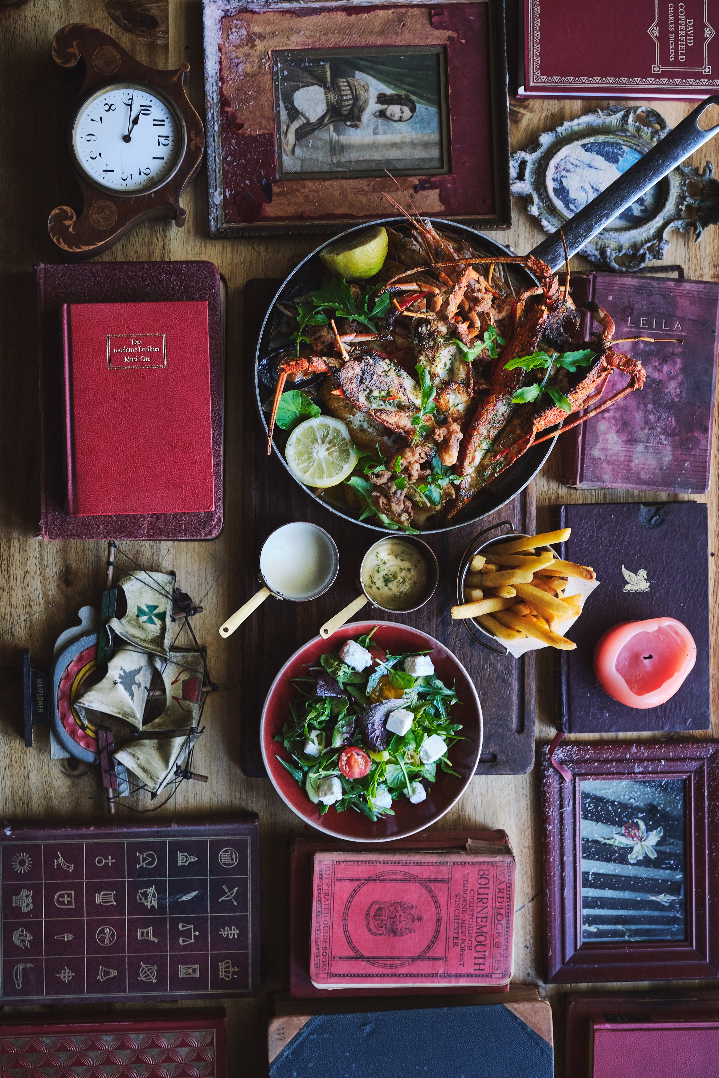 Tafel bij Kloof Street House met gegrilde kreeft, friet en salade tussen vintage boeken en decoraties.