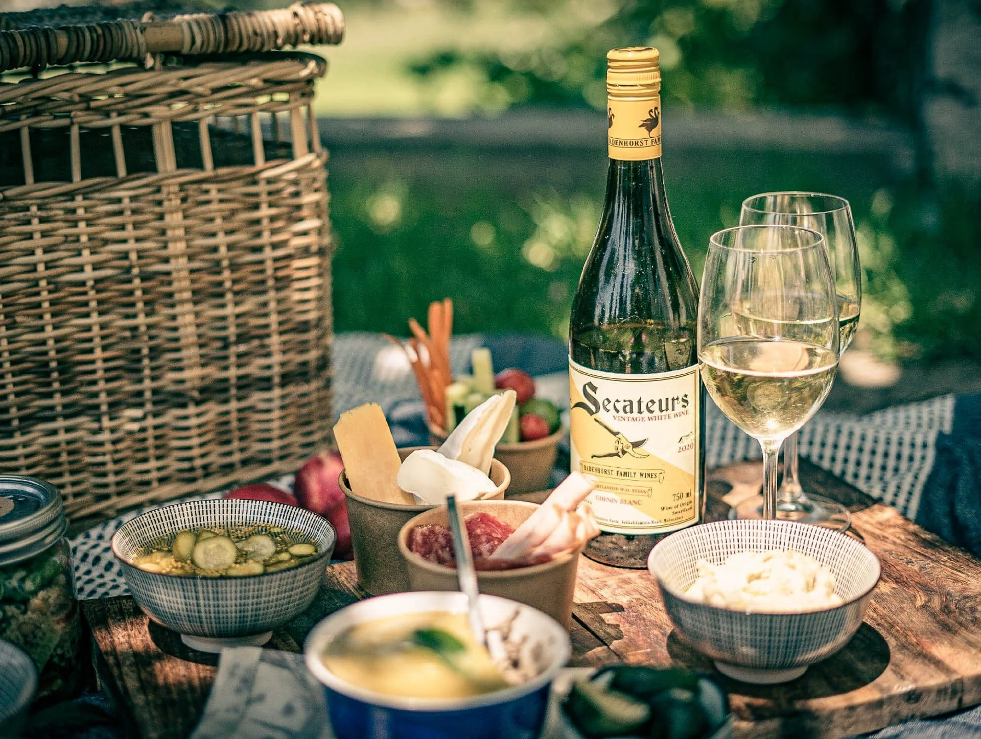 Picknicktafel met wijn, kazen en hapjes in een groene tuinsetting in Zuid-Afrika.