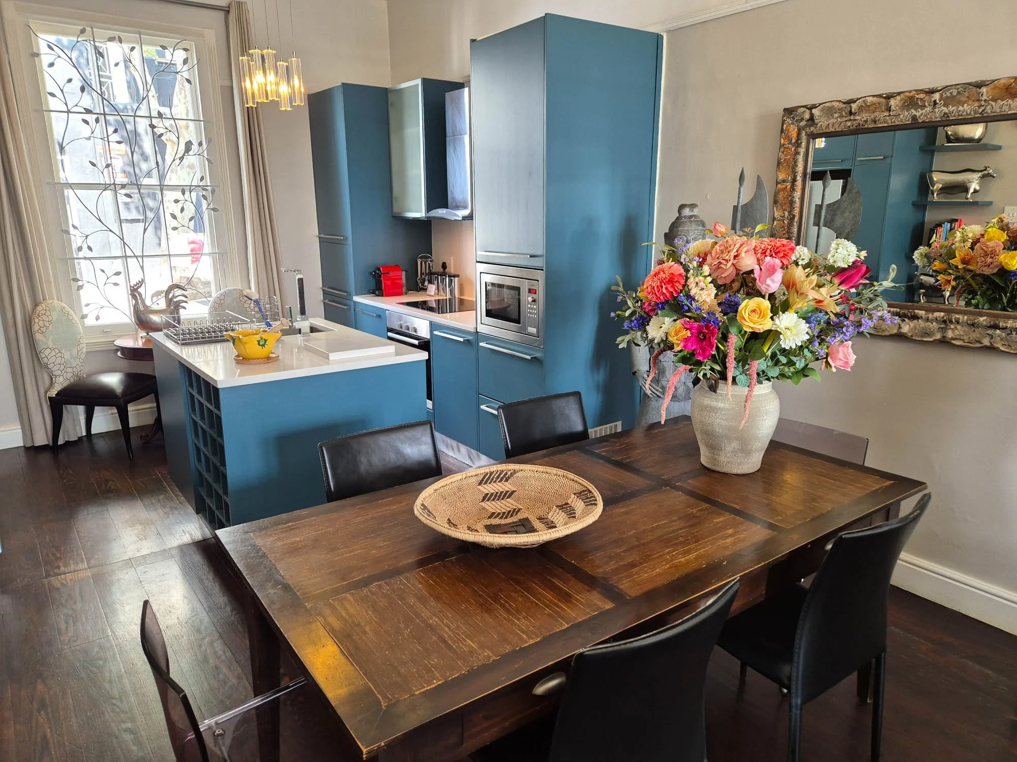 Blauwe keuken en houten eettafel met bloemen in een cottage in De Waterkant in Kaapstad.