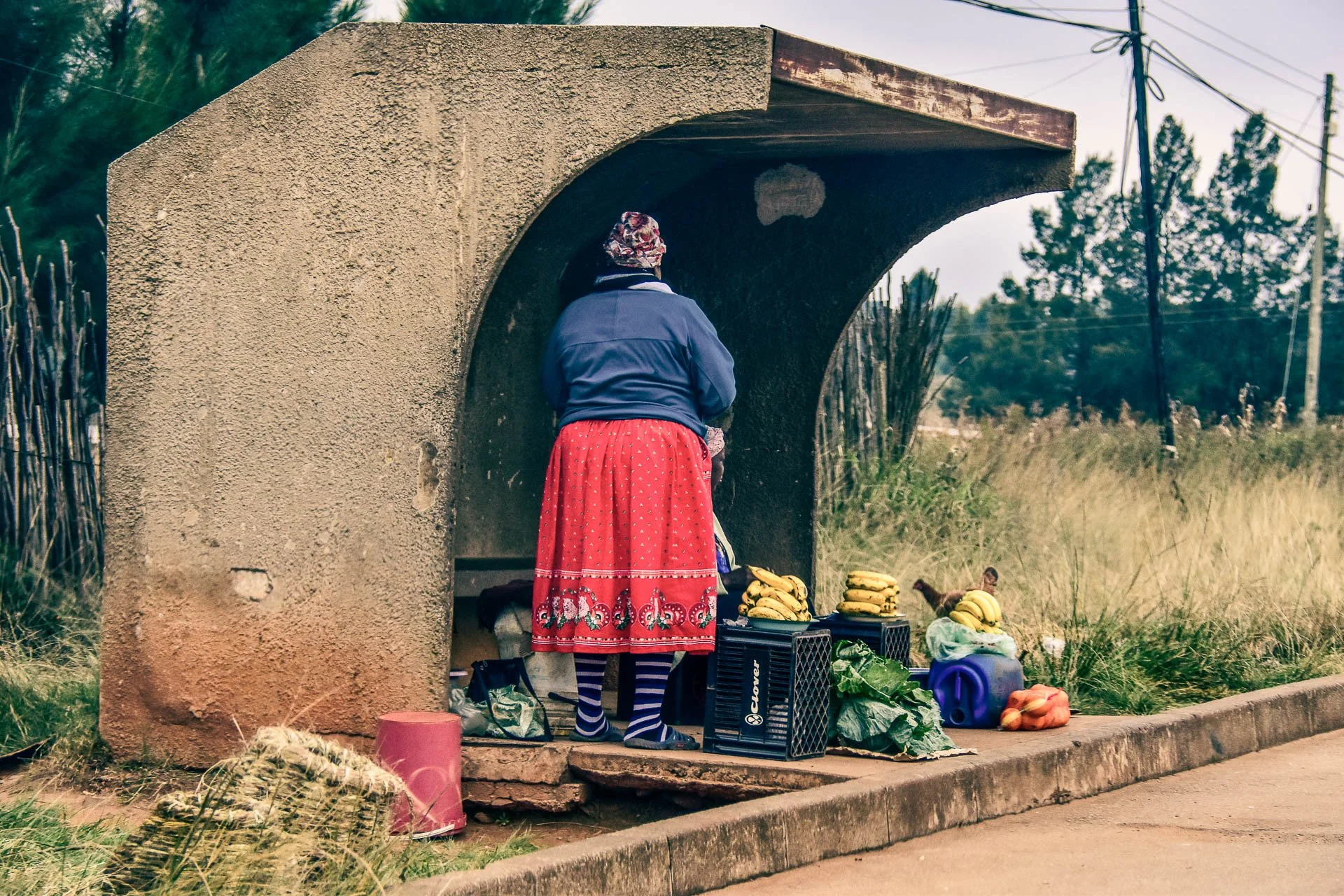Vrouw staat bij een eenvoudige bushalte met verse groente langs de weg in Zuid-Afrika.