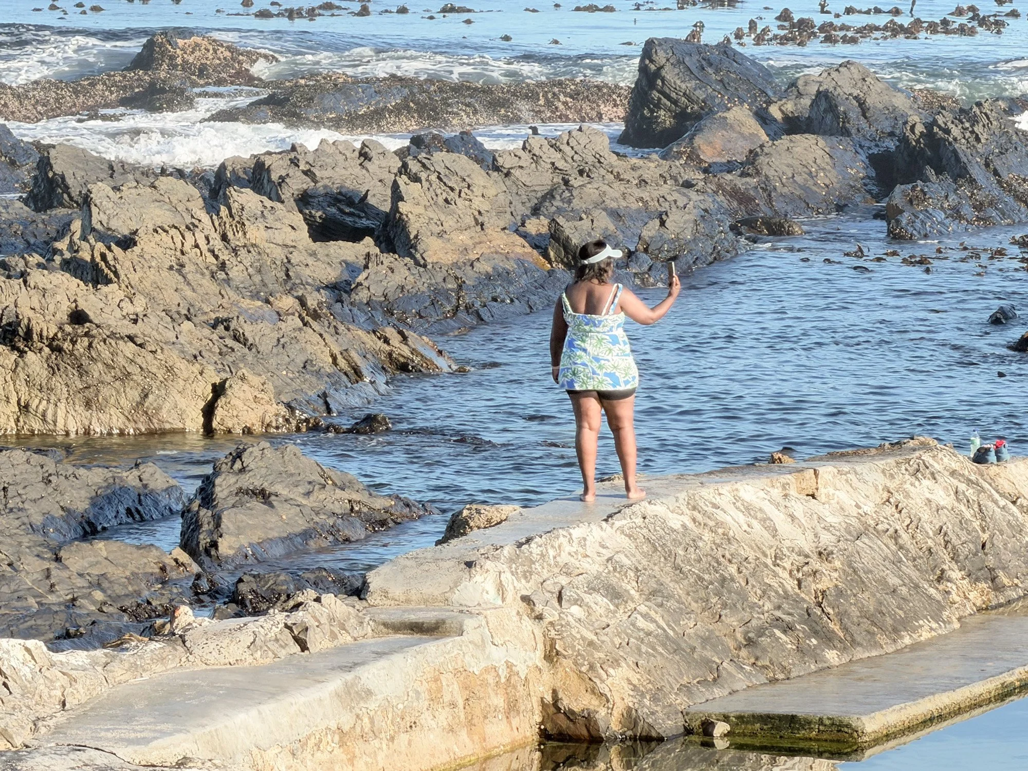 Vrouw die op rotsen aan zee staat en een selfie maakt tussen de golven in Seapoint, Zuid-Afrika.