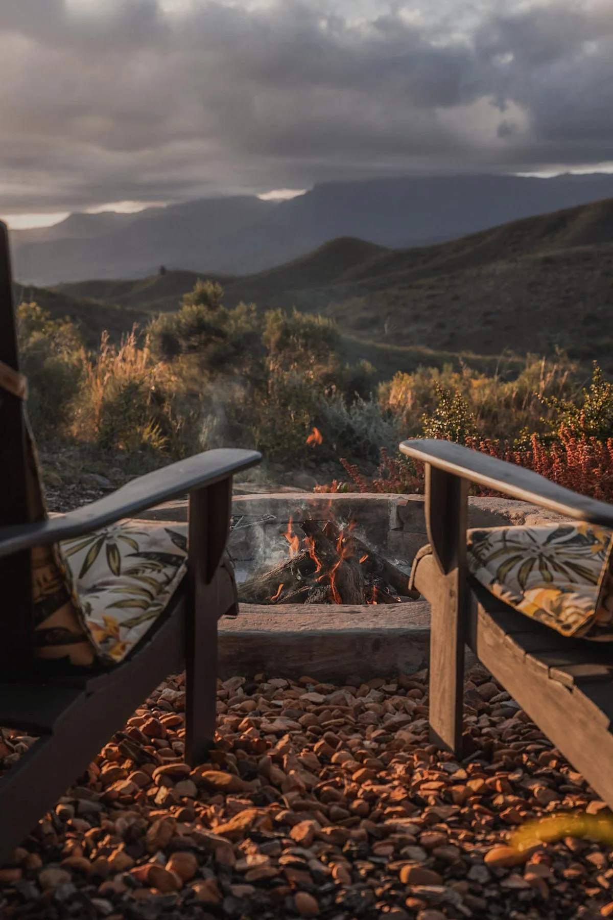 Twee stoelen bij vuurplaats van Aviary Hills met uitzicht op bergen en avondlucht in Zuid-Afrika.