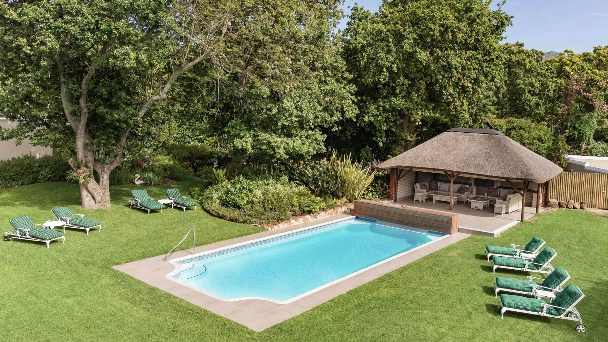 Zwembad van Glen Avon Hotel in een groene tuin met ligbedden en een rieten poolhouse.