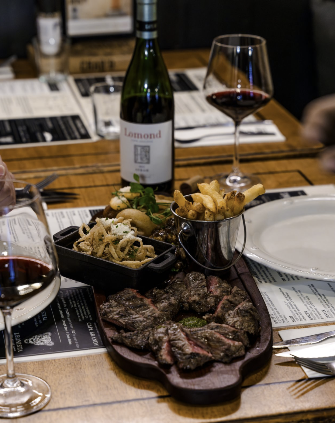 tafel met fles rode wijn Lomond, friet en dunne uiringen, biefstuk