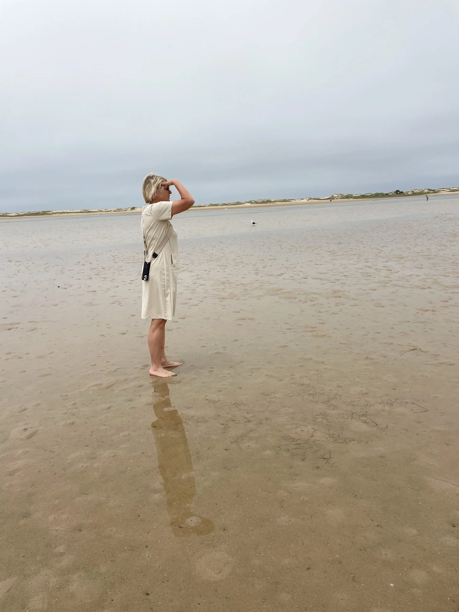 Vrouw staat op breed strand bij laagwater en kijkt over zee.