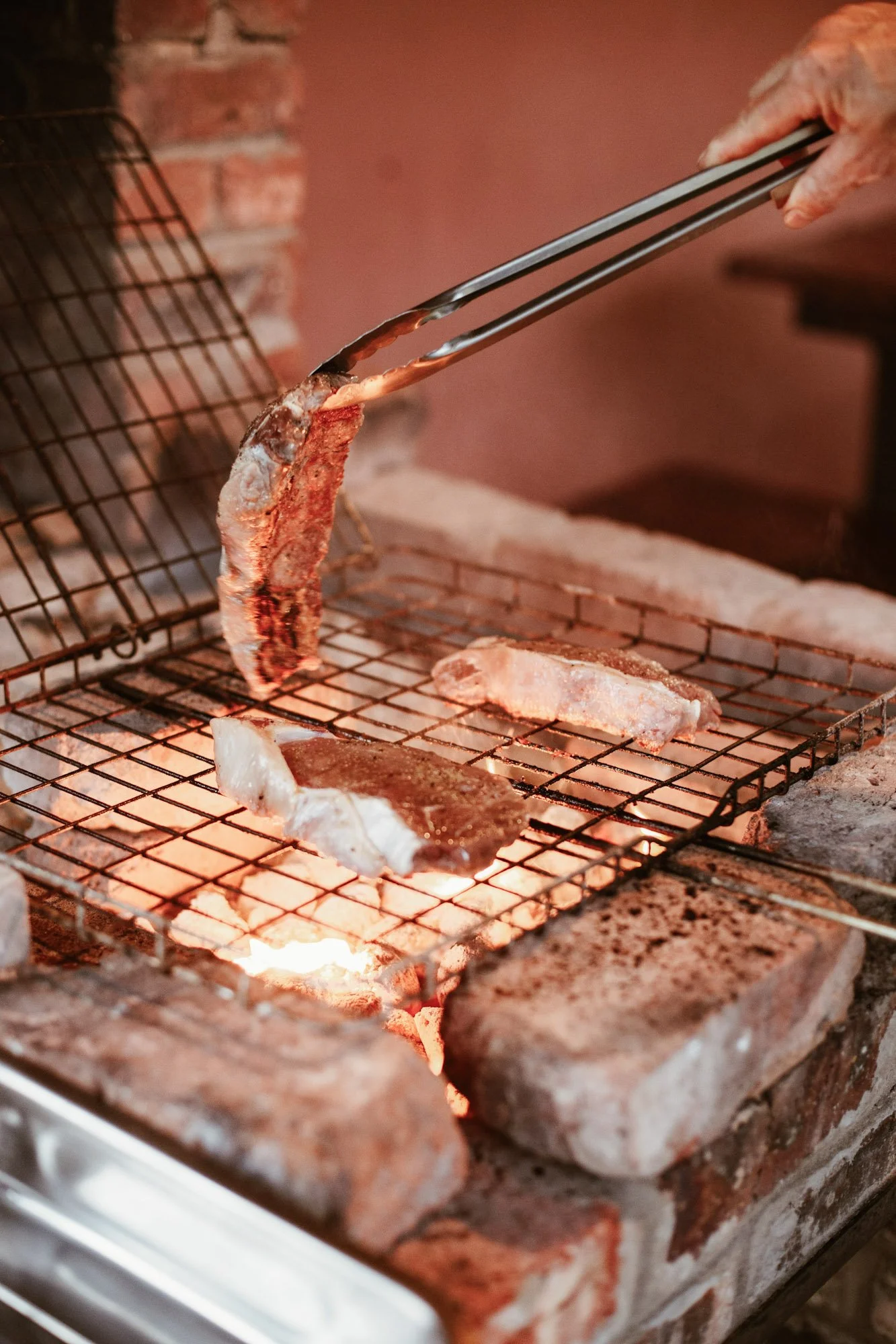 Iemand draait vlees om op een braai boven hete kolen.