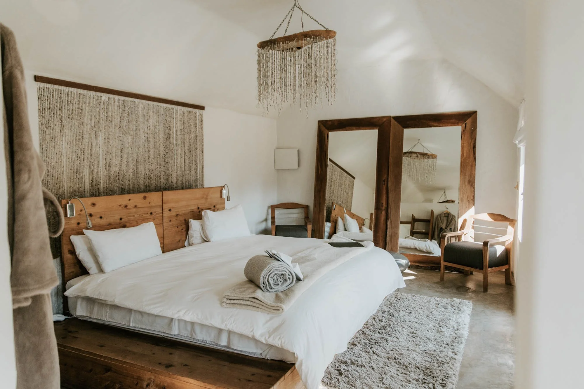 Ruime slaapkamer van Qambathi Mountain Lodge met wit beddengoed, houten meubels en grote spiegels.