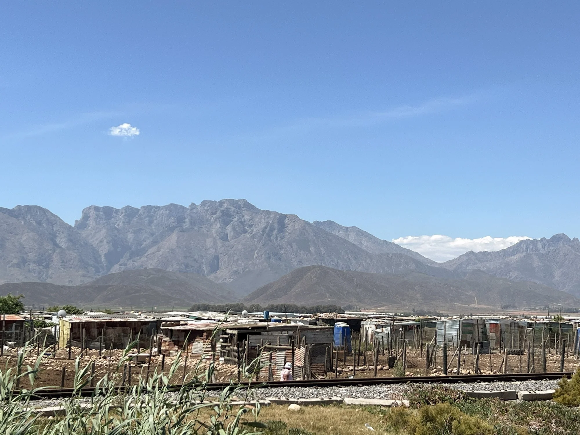 Eenvoudige huizen langs een spoorlijn met bergen op de achtergrond in Zuid-Afrika.
