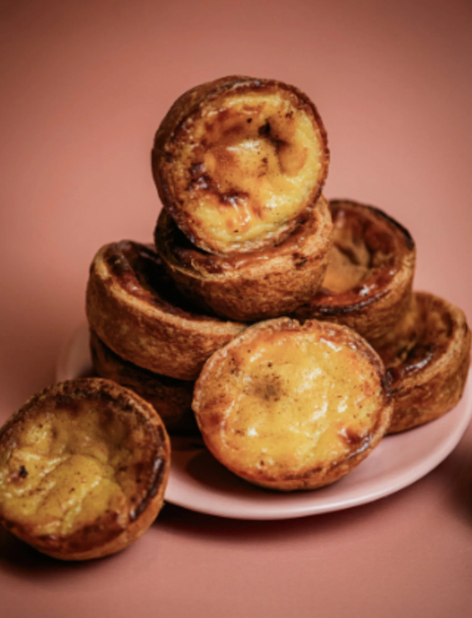 Stapel goudbruin gebakken pastéis de nata van Schoon op een roze achtergrond.