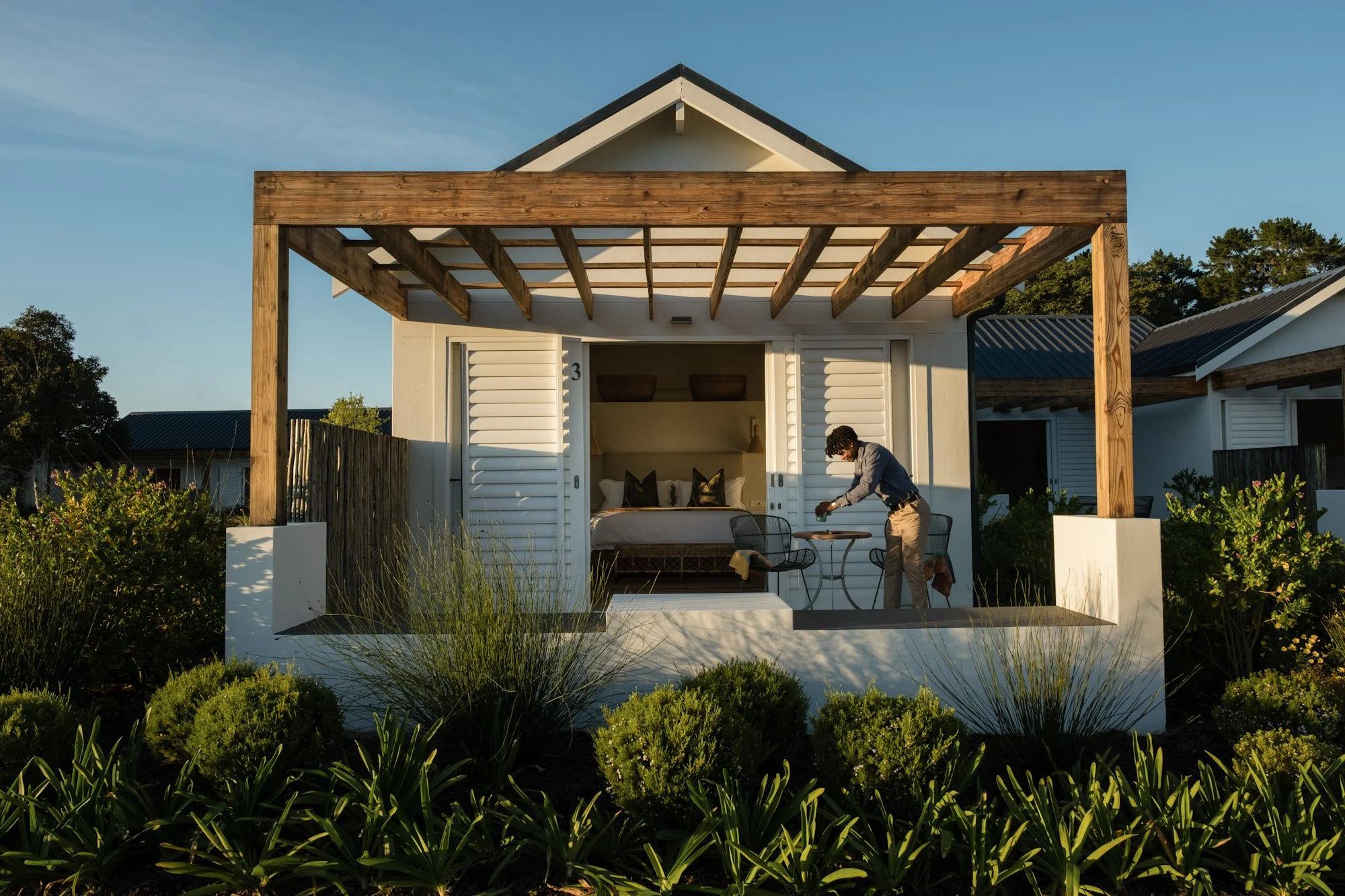 Vrijstaand cottage met houten veranda en persoon die tafel opmaakt in warm avondlicht