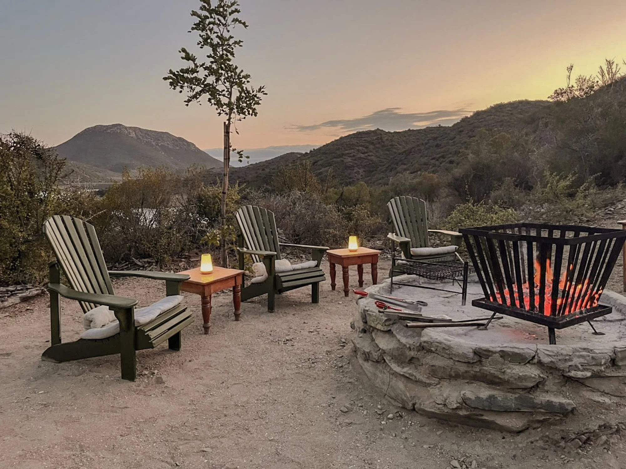 Vuurplaats met houten stoelen en uitzicht bij zonsondergang Tula Retreat in Zuid-Afrika.