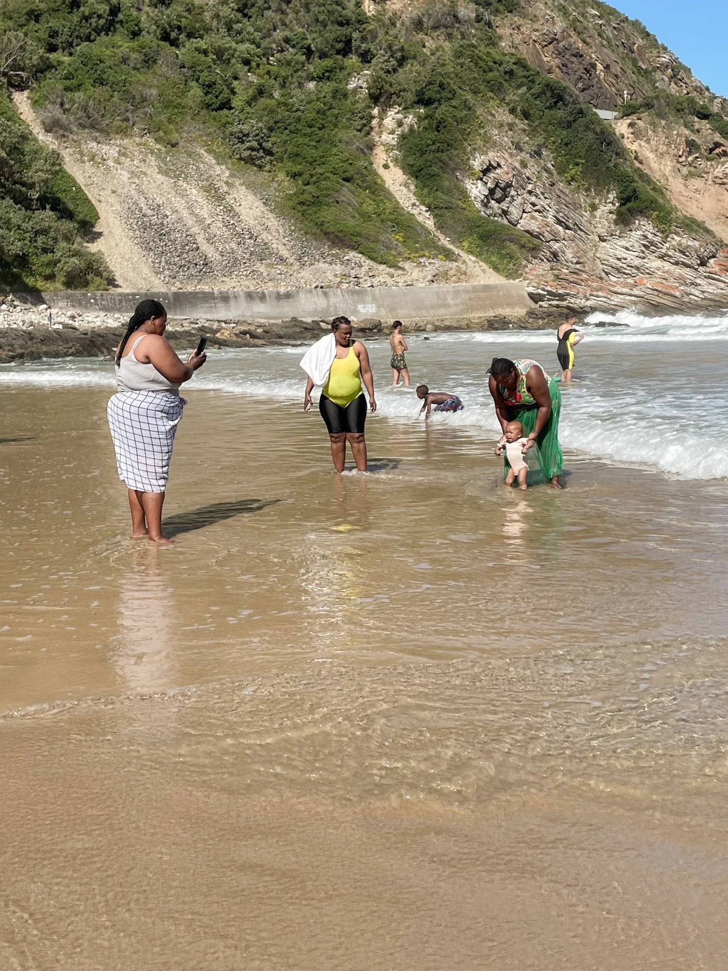Mensen spelen en zwemmen in zee bij rotsachtig strand in omgeving van Plettenberg Bay.