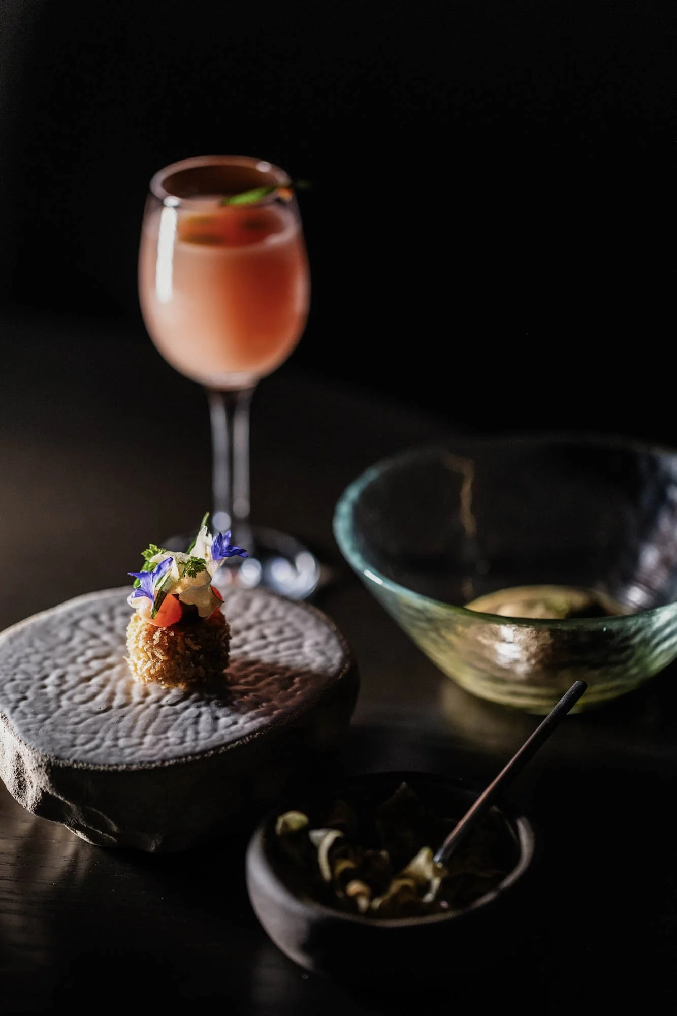 Verfijnde amuse met eetbare bloemen en een roze cocktail bij restaurant Mertia in Stellenbosch.