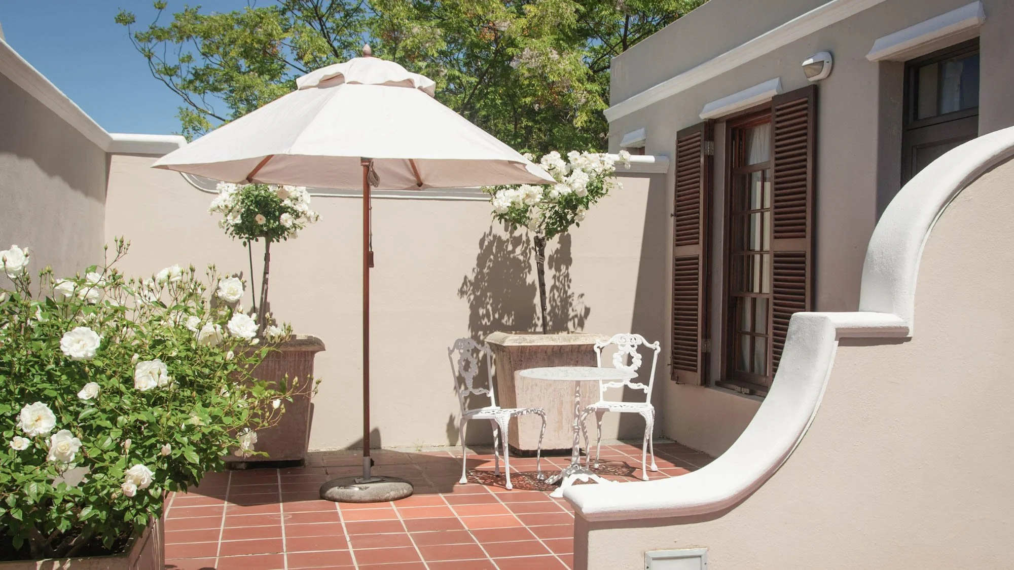 Privéterras van een kamer in Glen Avon Hotel met parasol, zitje en bloeiende witte rozen.