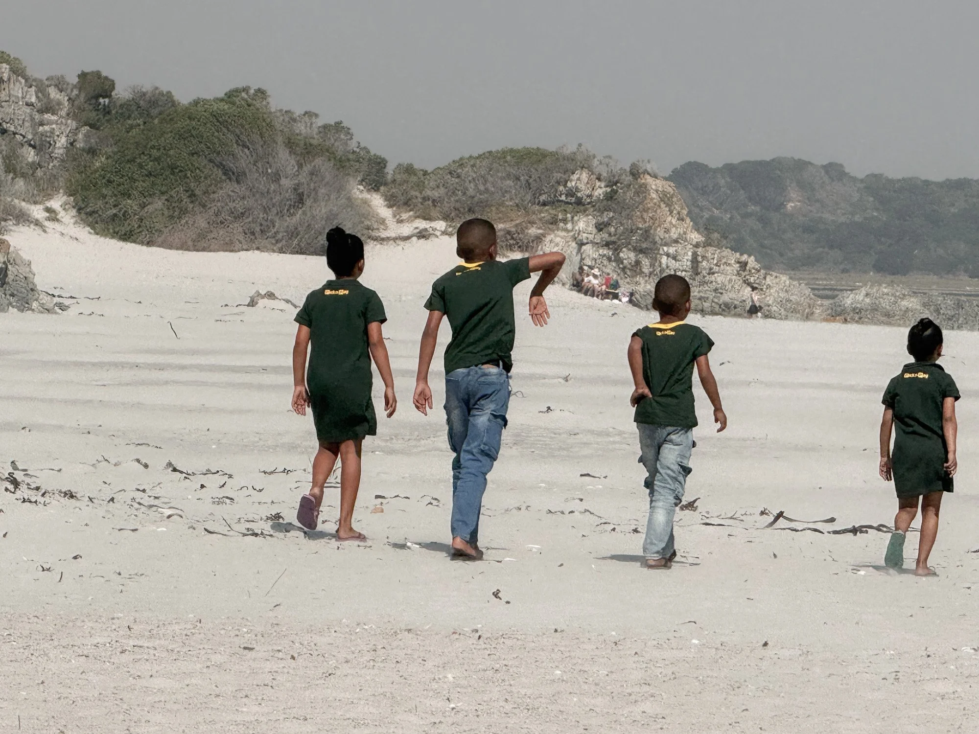 kinderen wandelen langs een leeg strand in Zuid-afrika