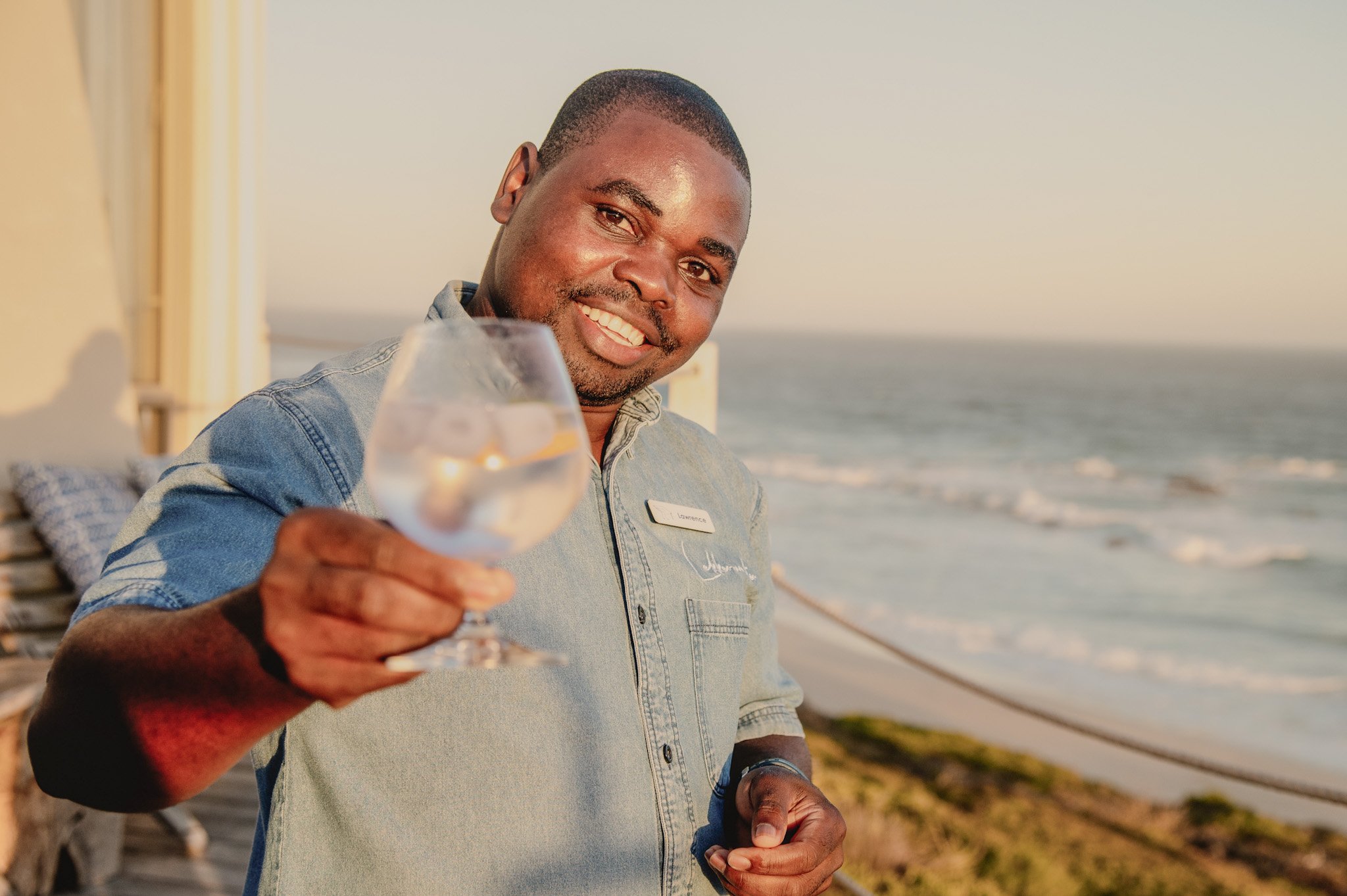 Medewerker van Lekkerwater Beach Lodge proost met een glas wijn met uitzicht op de oceaan in Zuid-Afrika