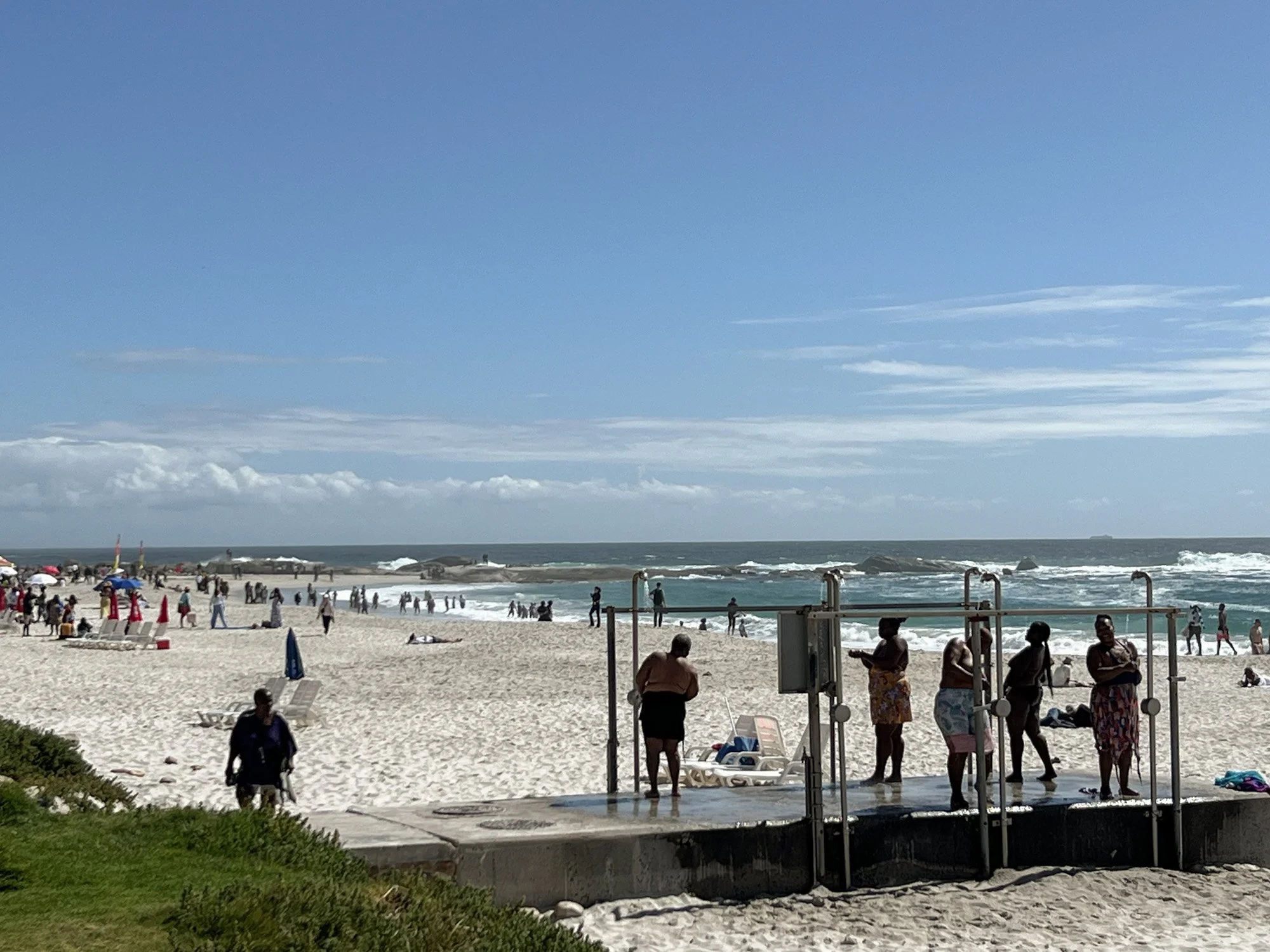 Mensen bij stranddouches in Camps Bay met zee op de achtergrond.
