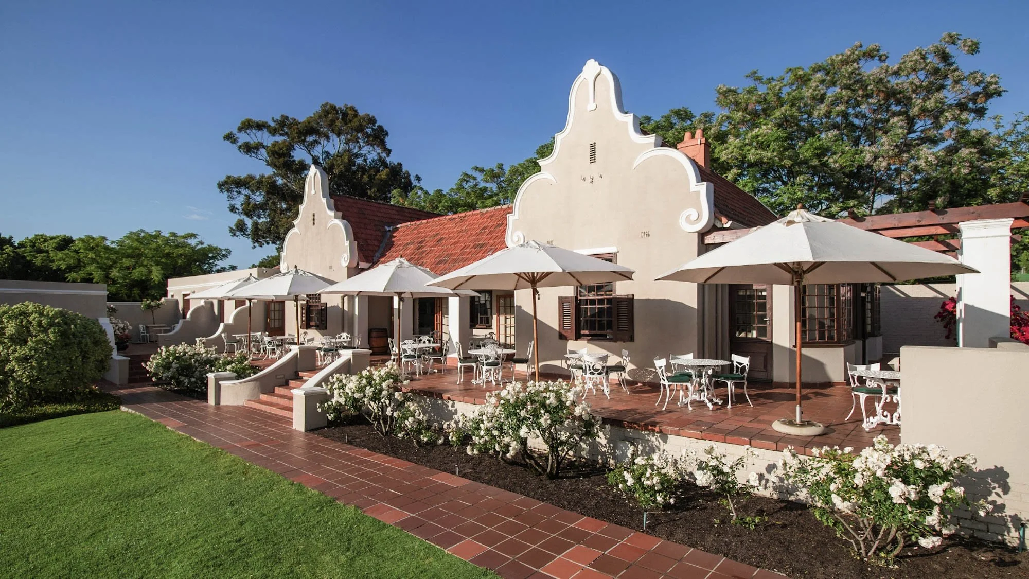 Terras en tuin van Glen Avon Hotel in Constantia met Kaaps-Hollandse gevels en witte rozen.