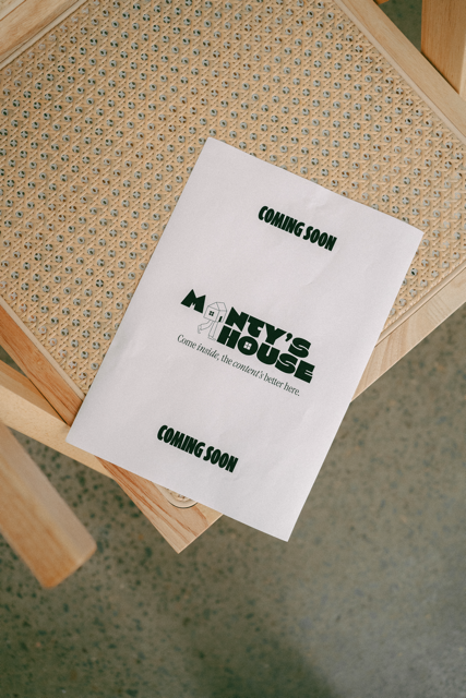 A paper sign on a chair with a cane woven seat, advertising the opening of 'Ney's House' with the words 'Coming Soon' at the top and bottom, and a tagline inviting people to come inside where the content is better.